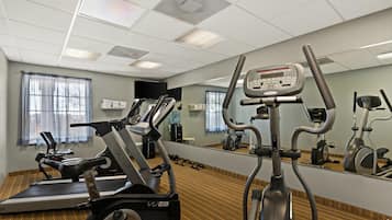 A gym with various exercise equipment, including treadmills and stationary bikes, and a large mirror reflecting the space.