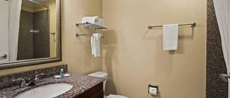 A bathroom with a granite countertop sink, a white toilet, a towel rack, and a mirror.