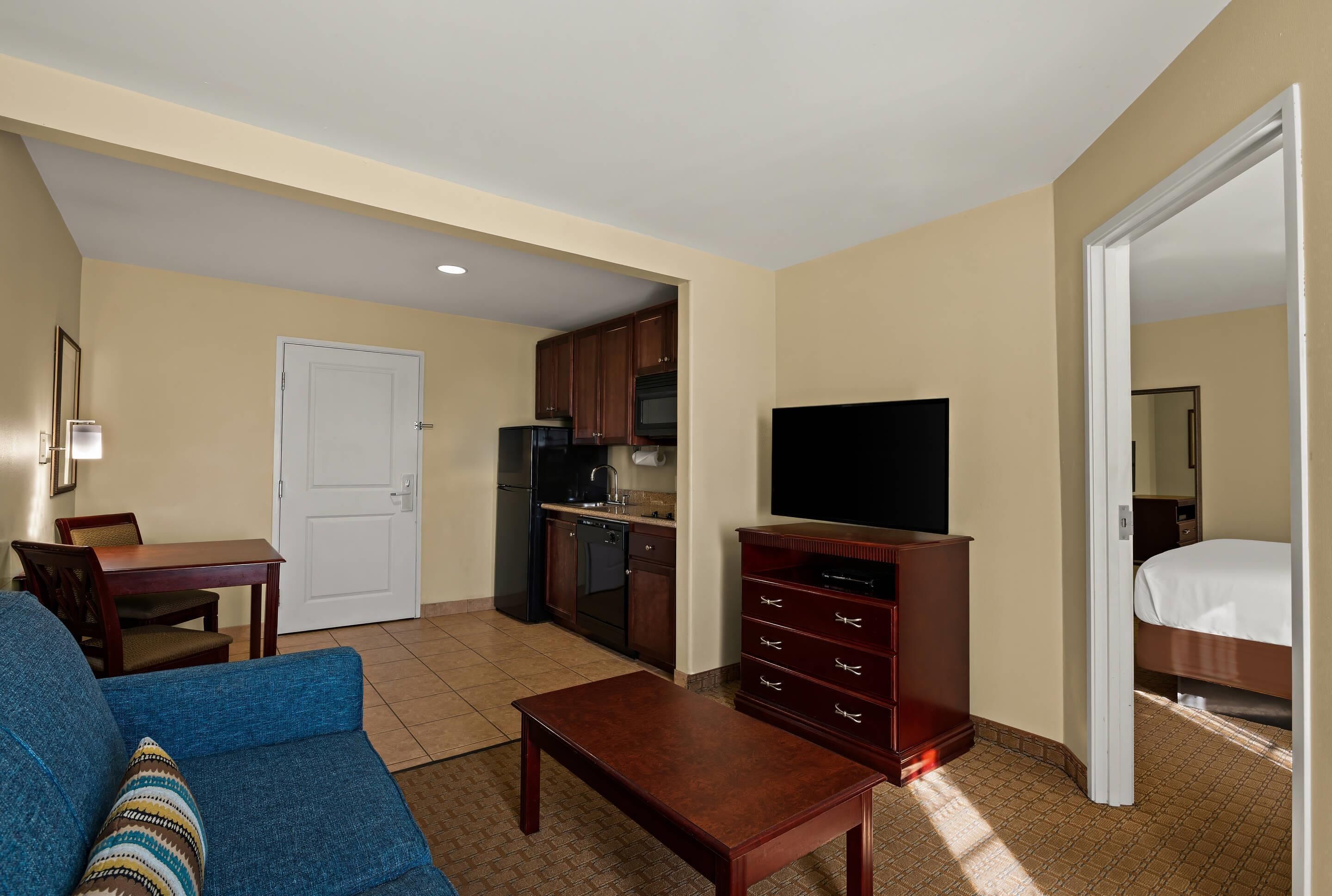 Een compacte hotelkamer met kitchenette, flatscreen televisie, een sofa en een bed.