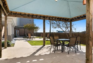 A covered patio area with a table and chairs, a concrete pathway, and a wooden fence in the background.