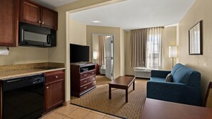 A compact hotel room with a kitchenette, a flat-screen TV, a sofa, and a dining table. - MainStay Suites Houma (Houma)
