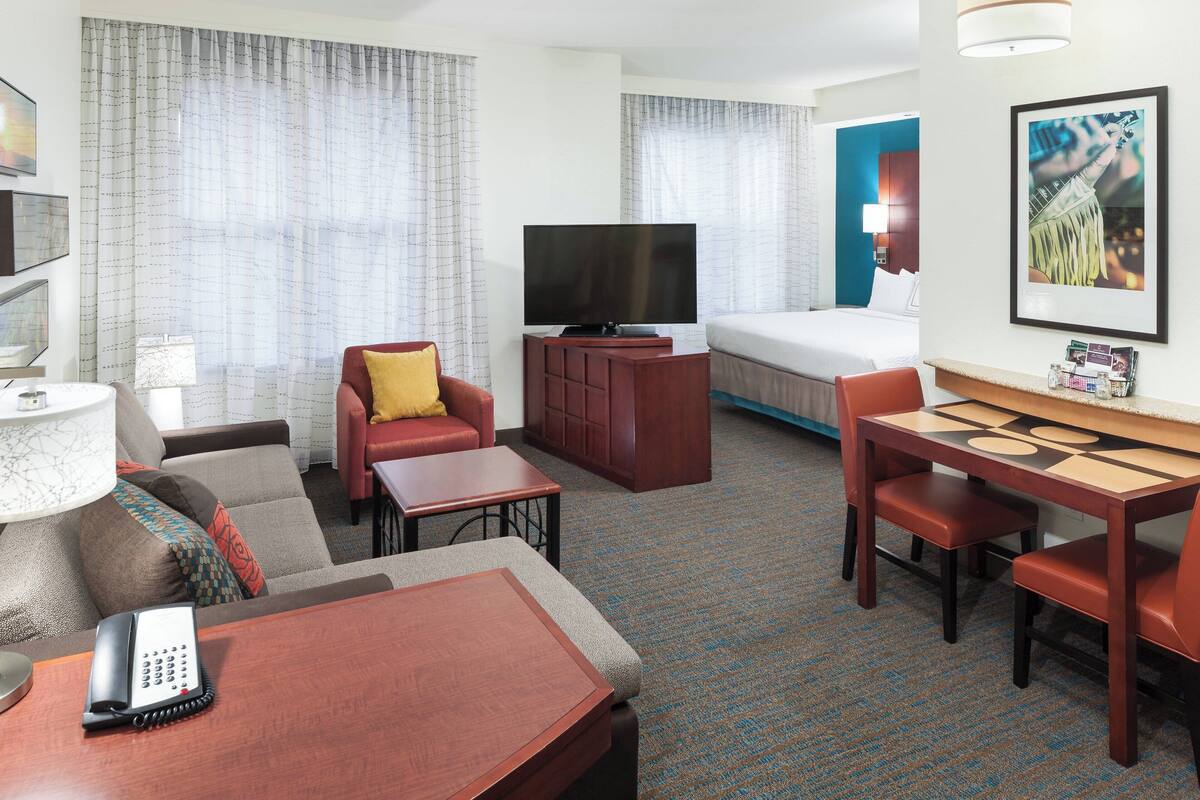 Habitación de hotel con cama, televisión, escritorio con silla, sofá y teléfono.