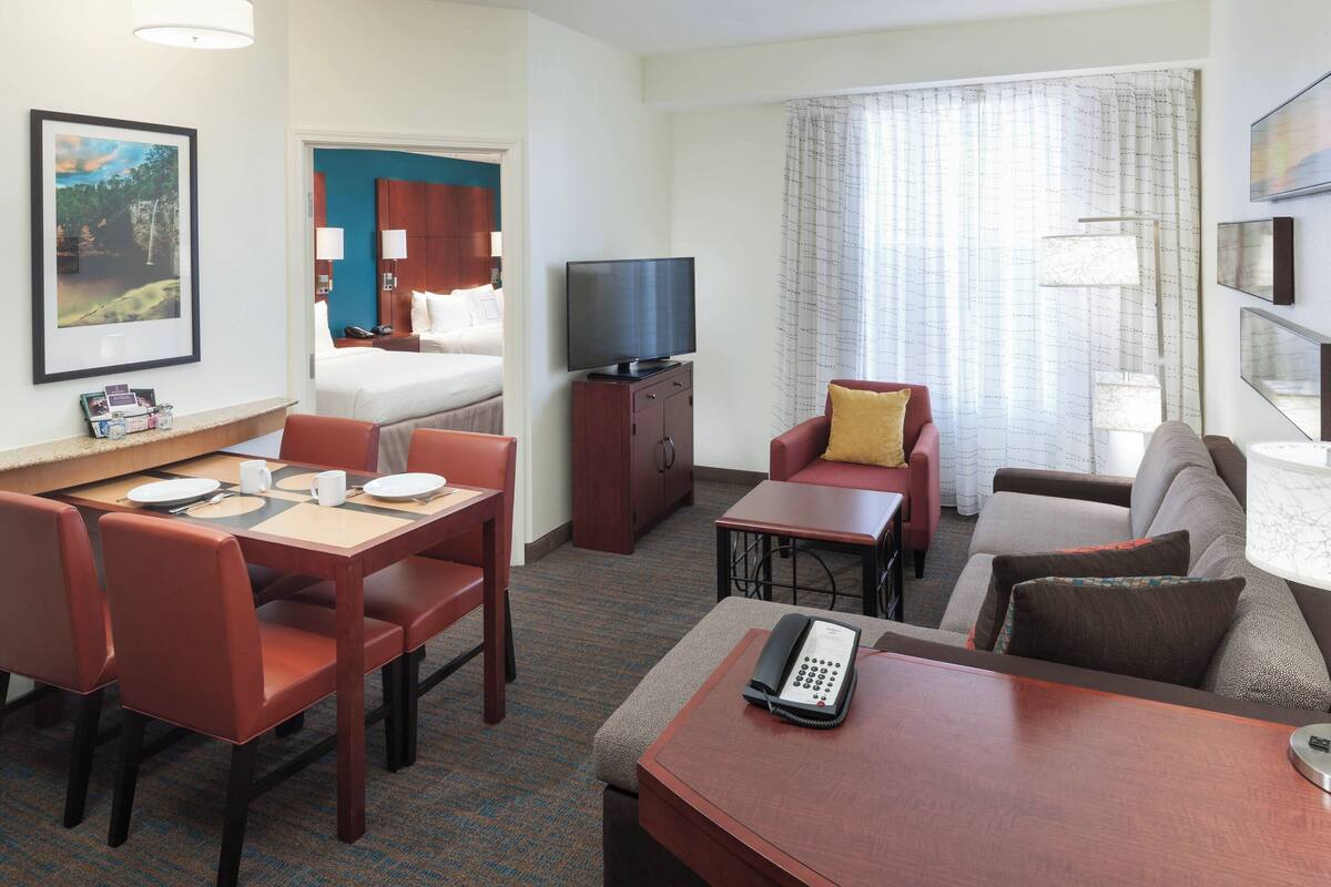 Habitación de hotel con cama, televisión, escritorio con teléfono, zona de comedor con sillas y sofá.