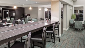 A modern hotel lobby with a long counter, comfortable seating, and a large window providing natural light.