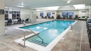 An indoor swimming pool with a tiled floor, lounge chairs, and a no diving sign.