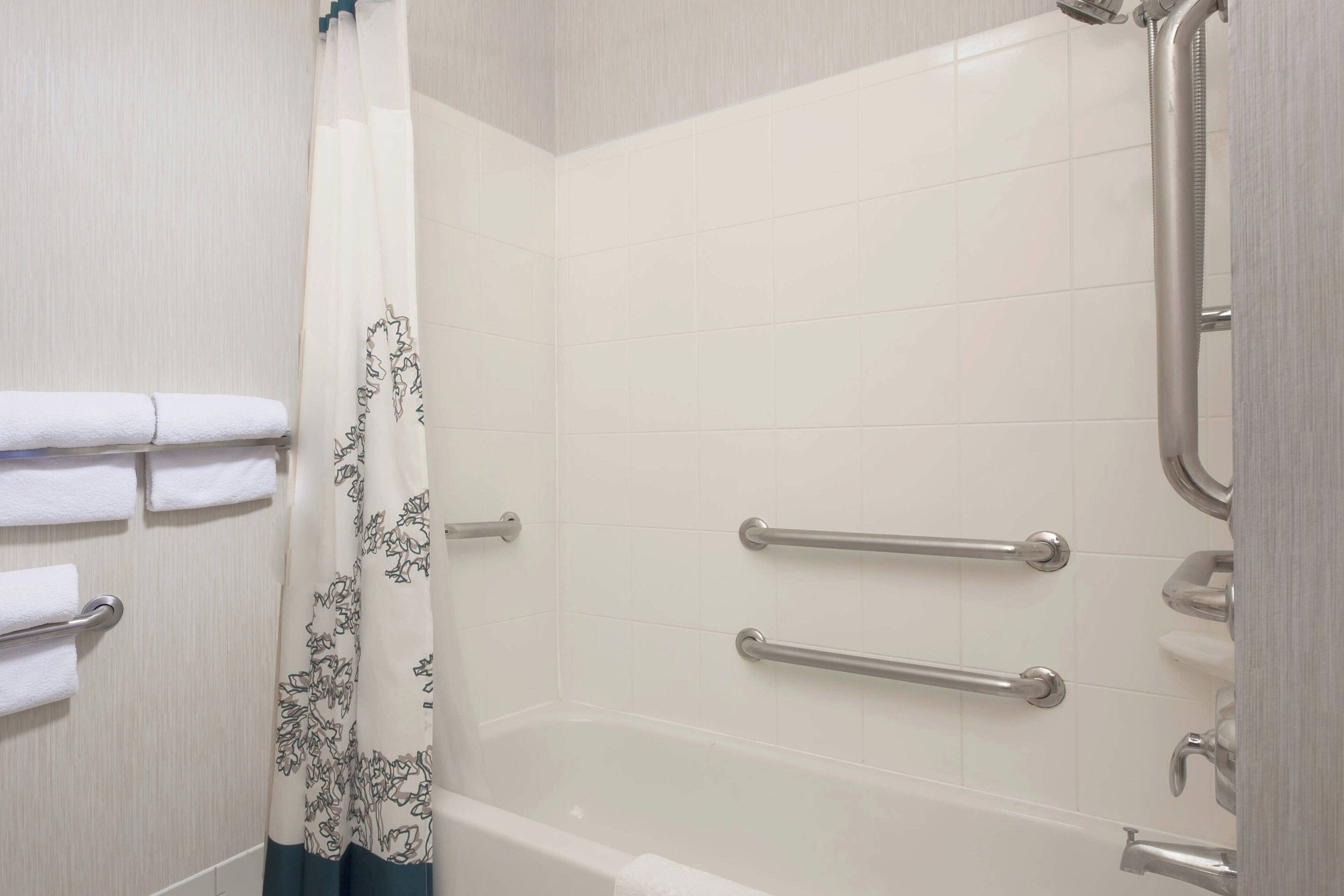 A bathroom with a bathtub, grab bars, and a shower curtain.