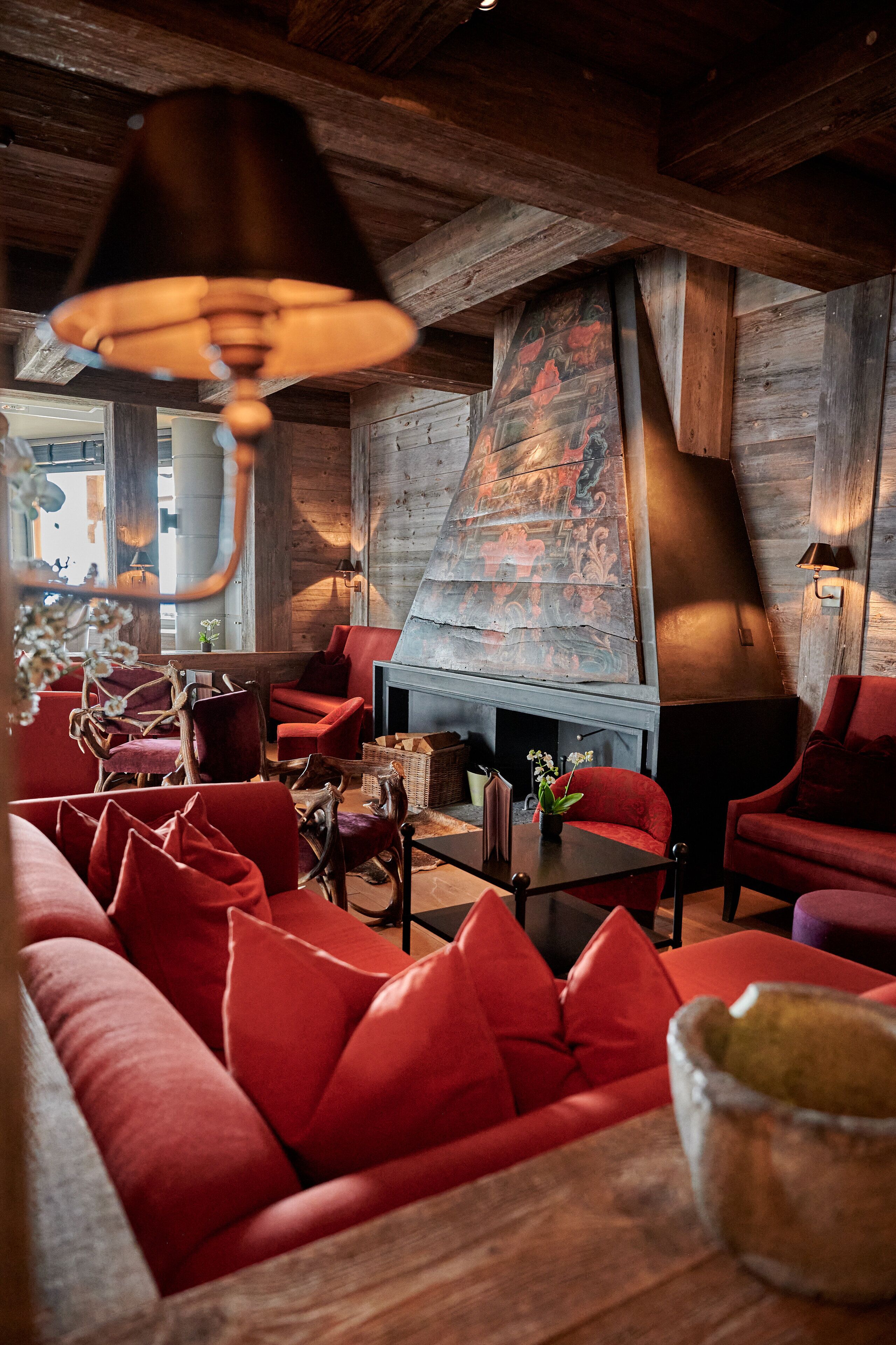 A cozy interior with red upholstered seating, a large fireplace, and wooden beams.