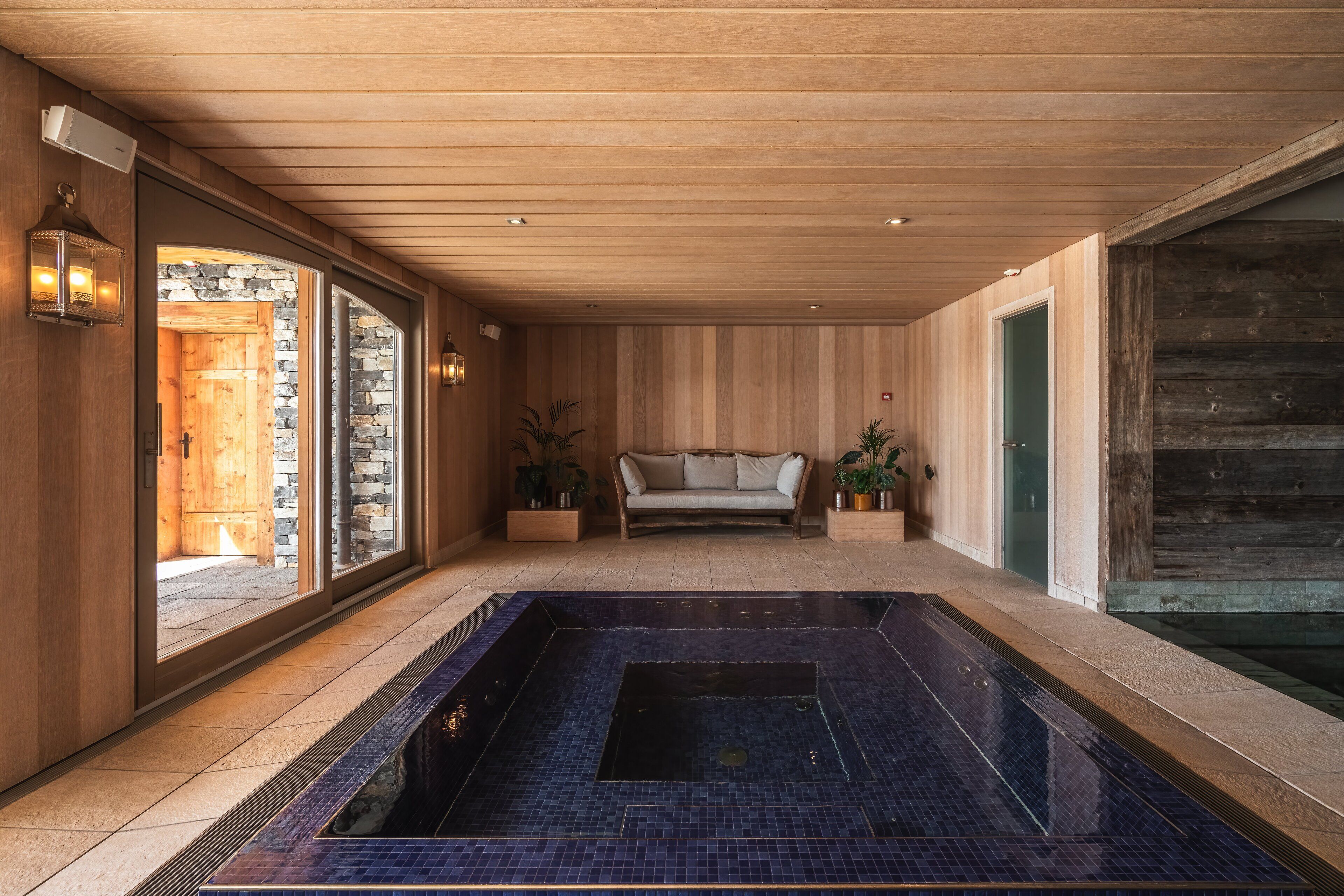 Ein Wellnessbereich mit Whirlpool, Holzwänden, einer Couch und Topfpflanzen.