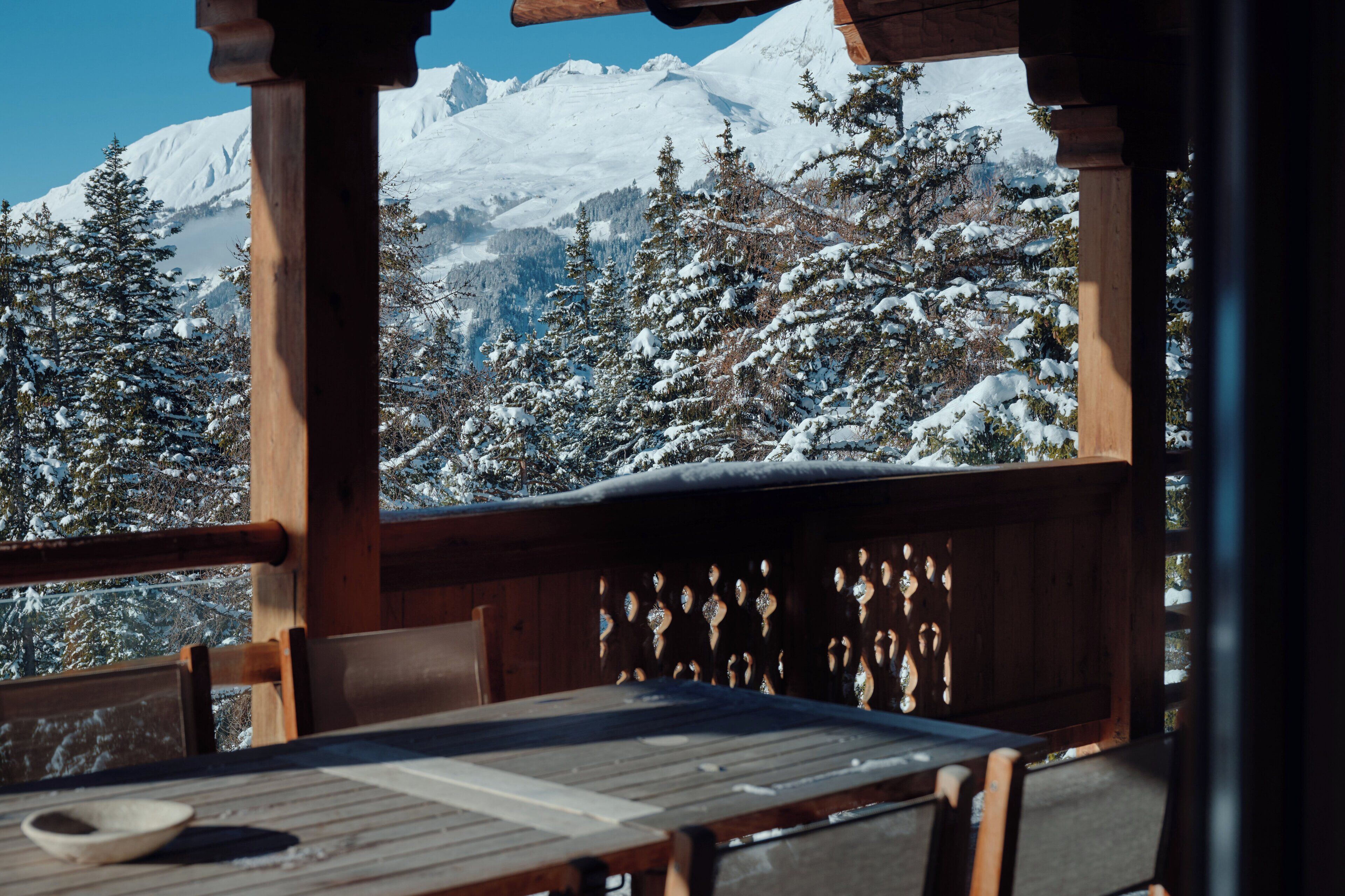 Um deck de madeira com mesa e cadeiras, com vista para uma paisagem montanhosa coberta de neve.