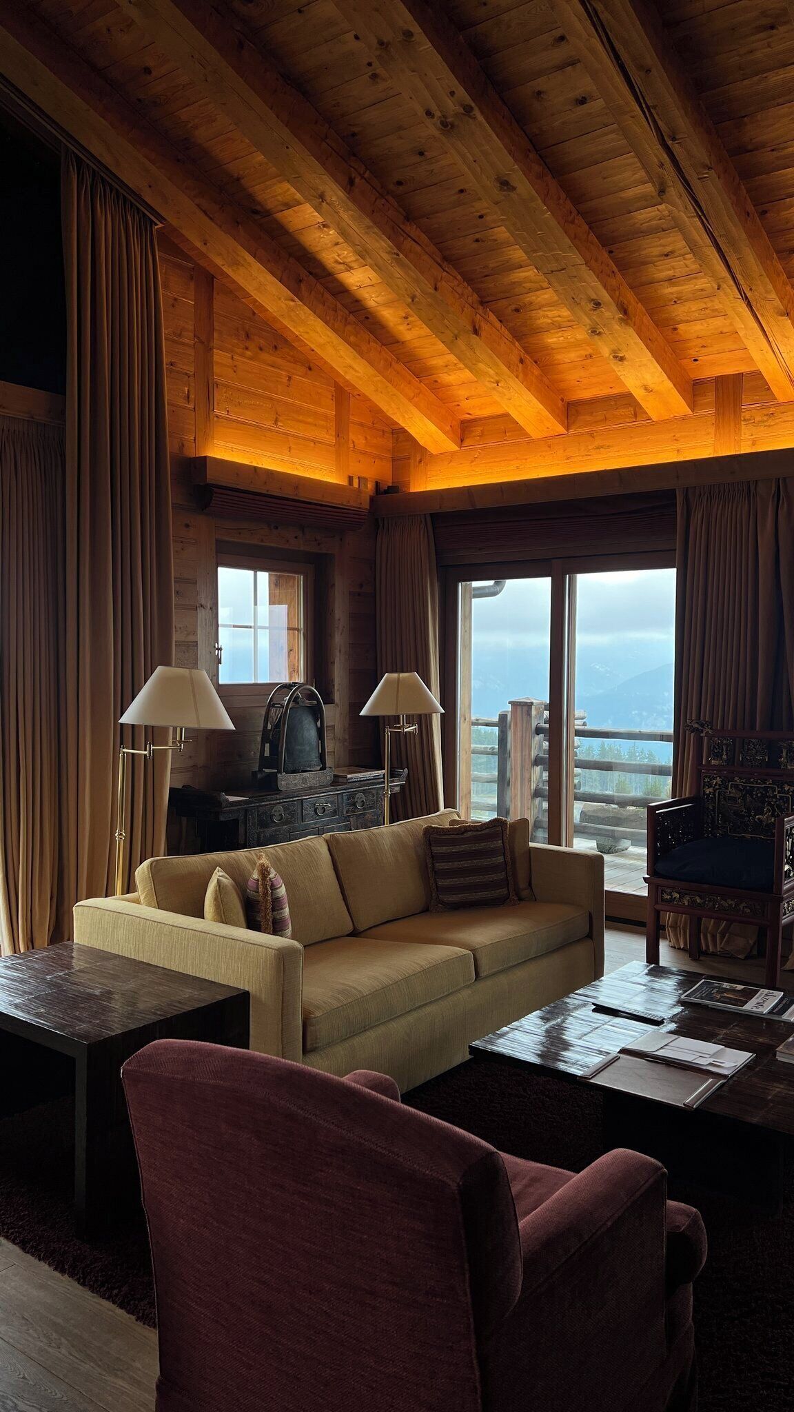 A cozy cabin interior with a wooden ceiling, a sofa, a chair, and a table.