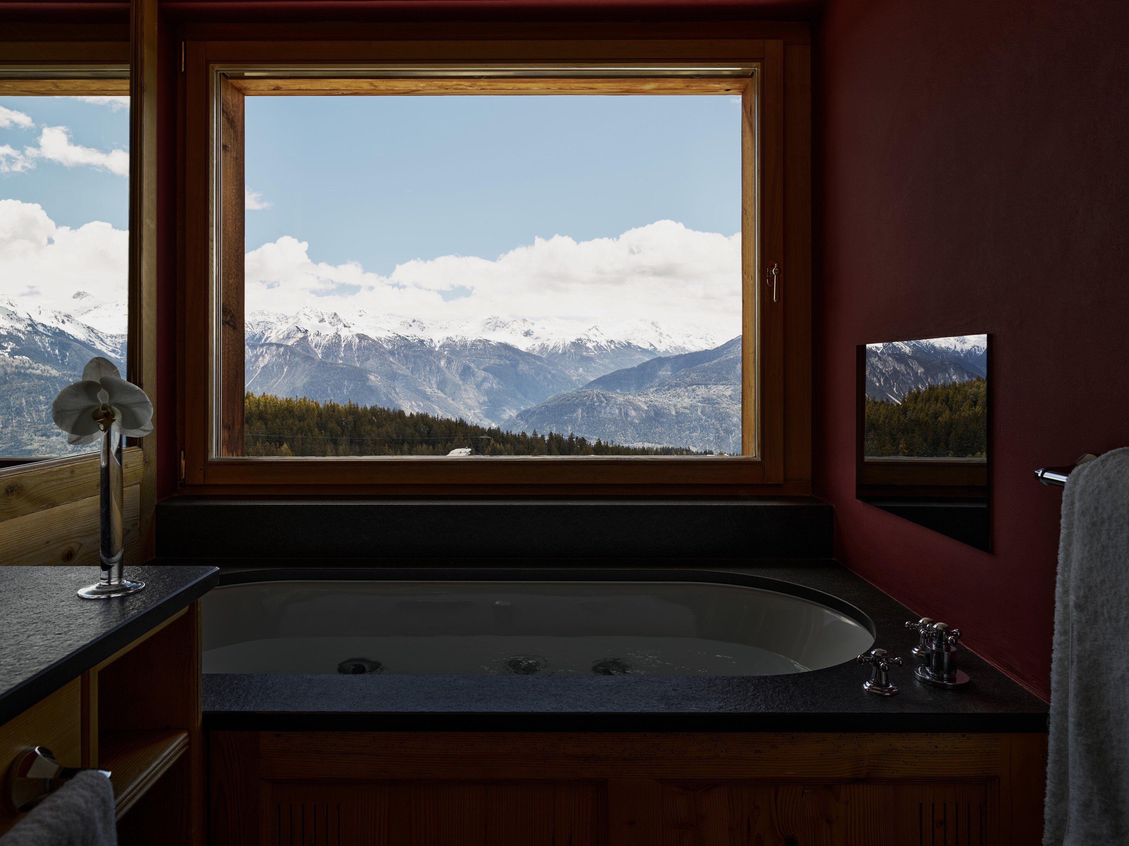A bathroom with a large window, a bathtub, and a mirror.