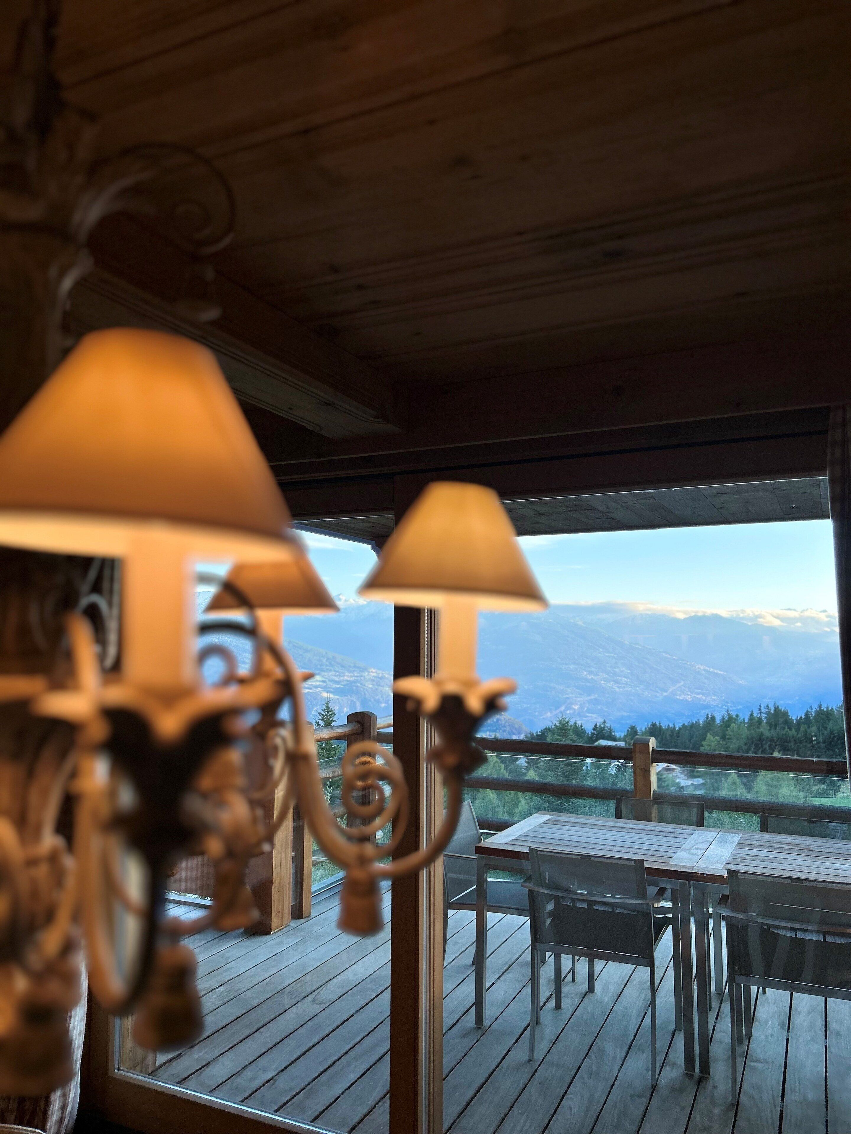 A wooden deck with a table and chairs, overlooking a mountainous landscape.