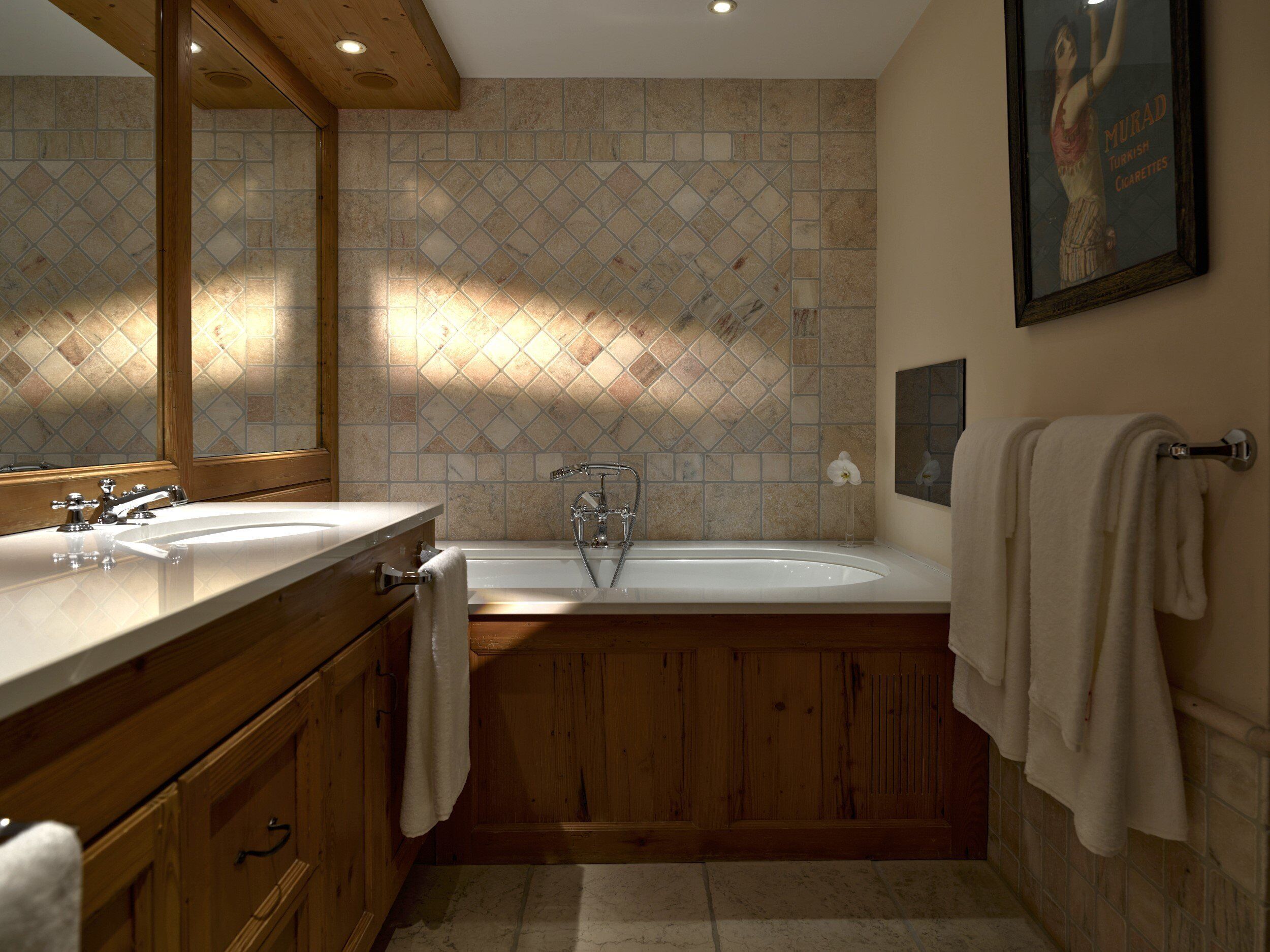 A bathroom with two sinks, a bathtub, wooden cabinets, and a tiled wall.