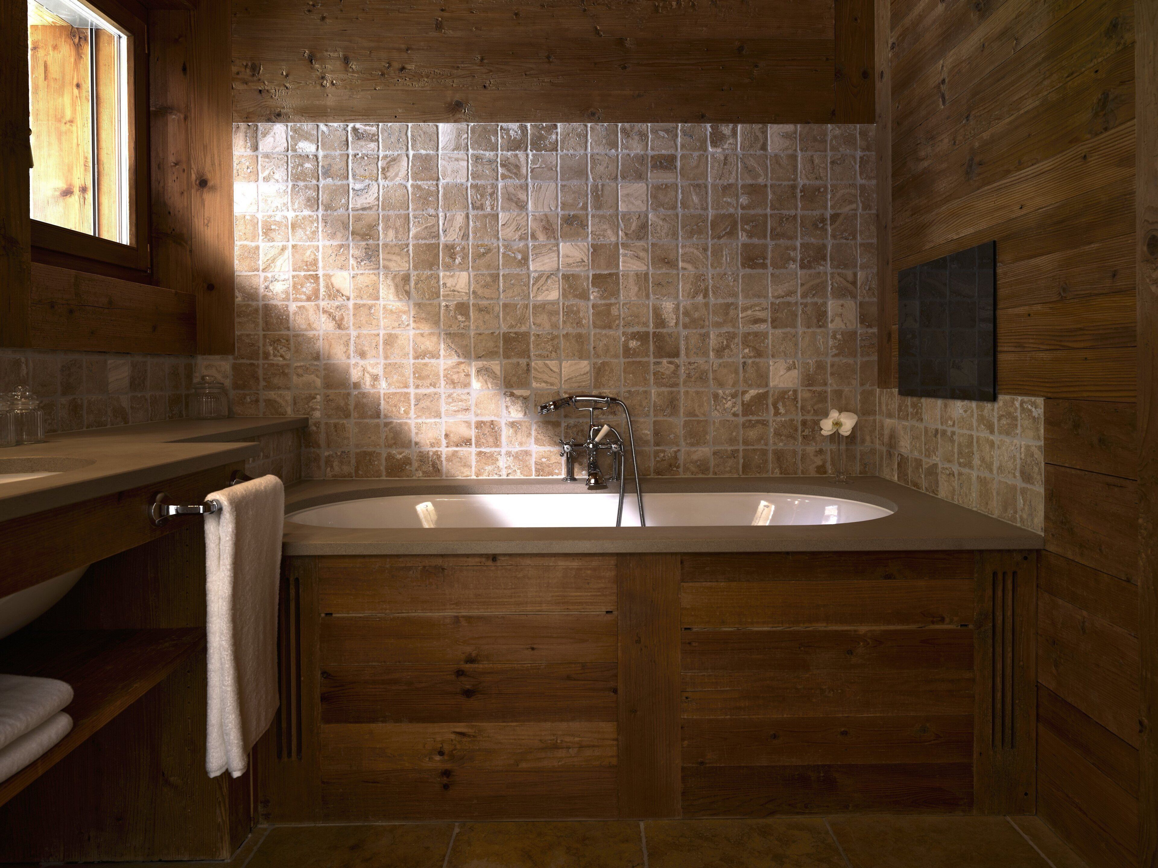 Un baño de madera con una bañera independiente, un ventanal y un muro con azulejos.
