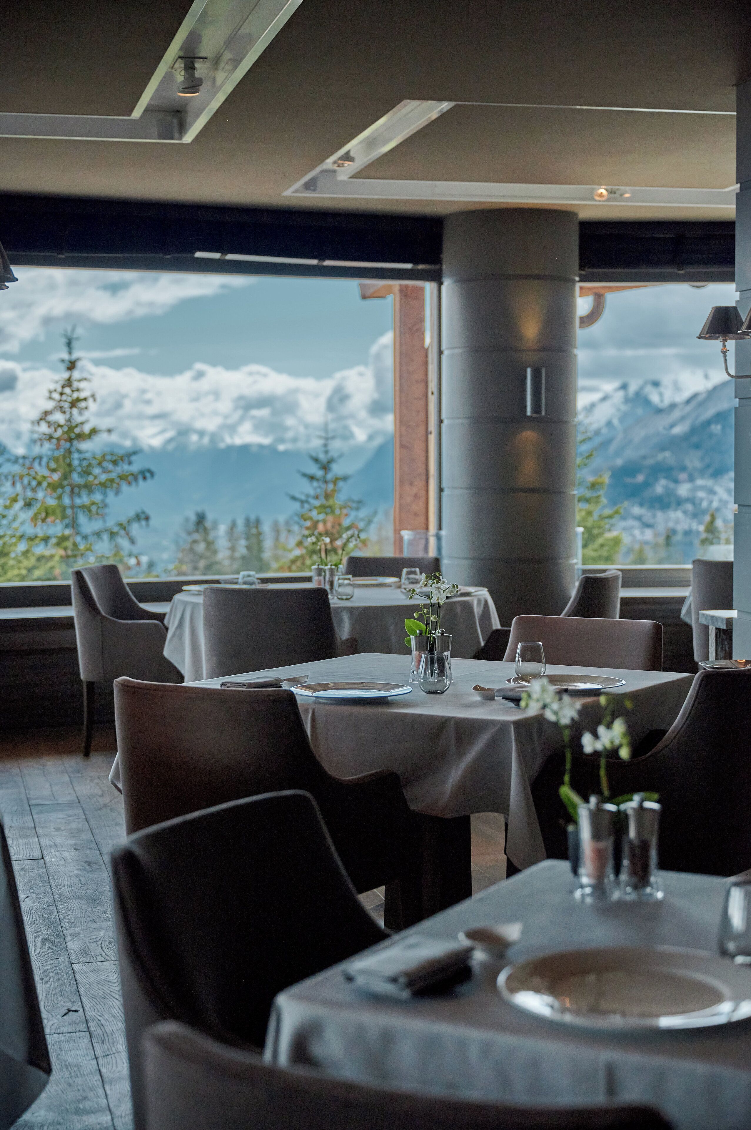 A restaurant with tables set for dining, large windows offering a mountain view, and modern interior design.