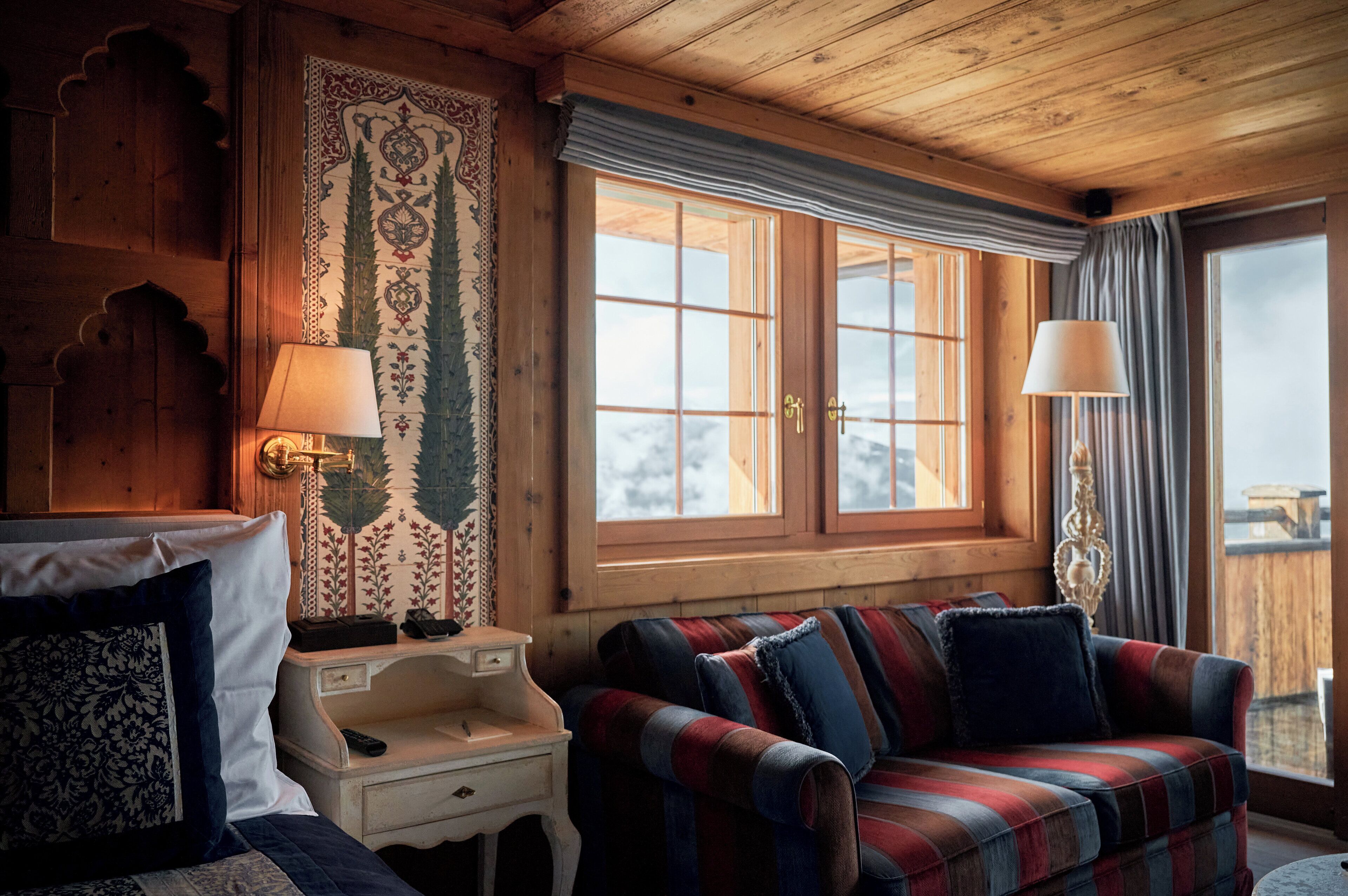 A cozy room with a plaid sofa, a wooden headboard, and a large window with curtains.