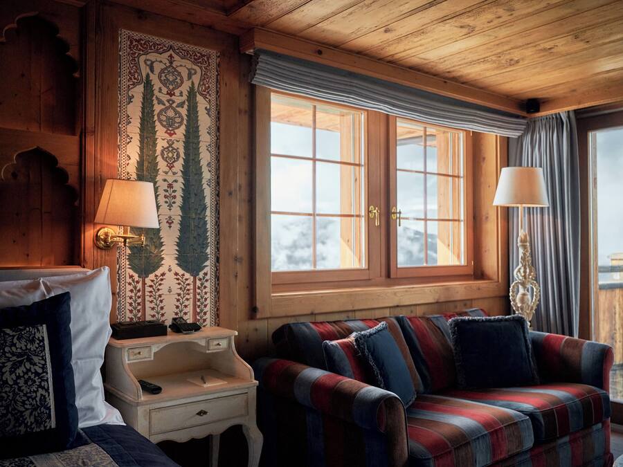 A cozy room with a plaid sofa, a wooden headboard, and a large window with curtains.