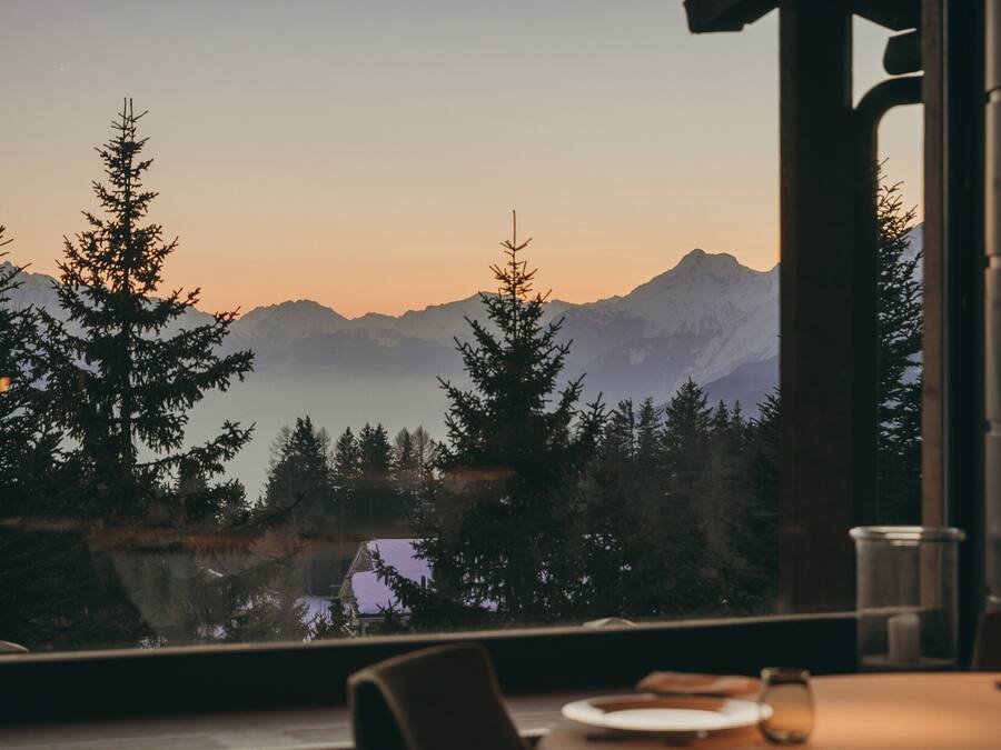 A dining area with a table set for two, overlooking a mountainous landscape.