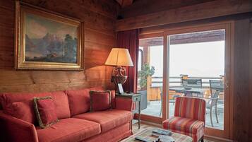 A wooden interior with a sofa, a lamp, a painting, and a view through a glass door to an outdoor seating area.