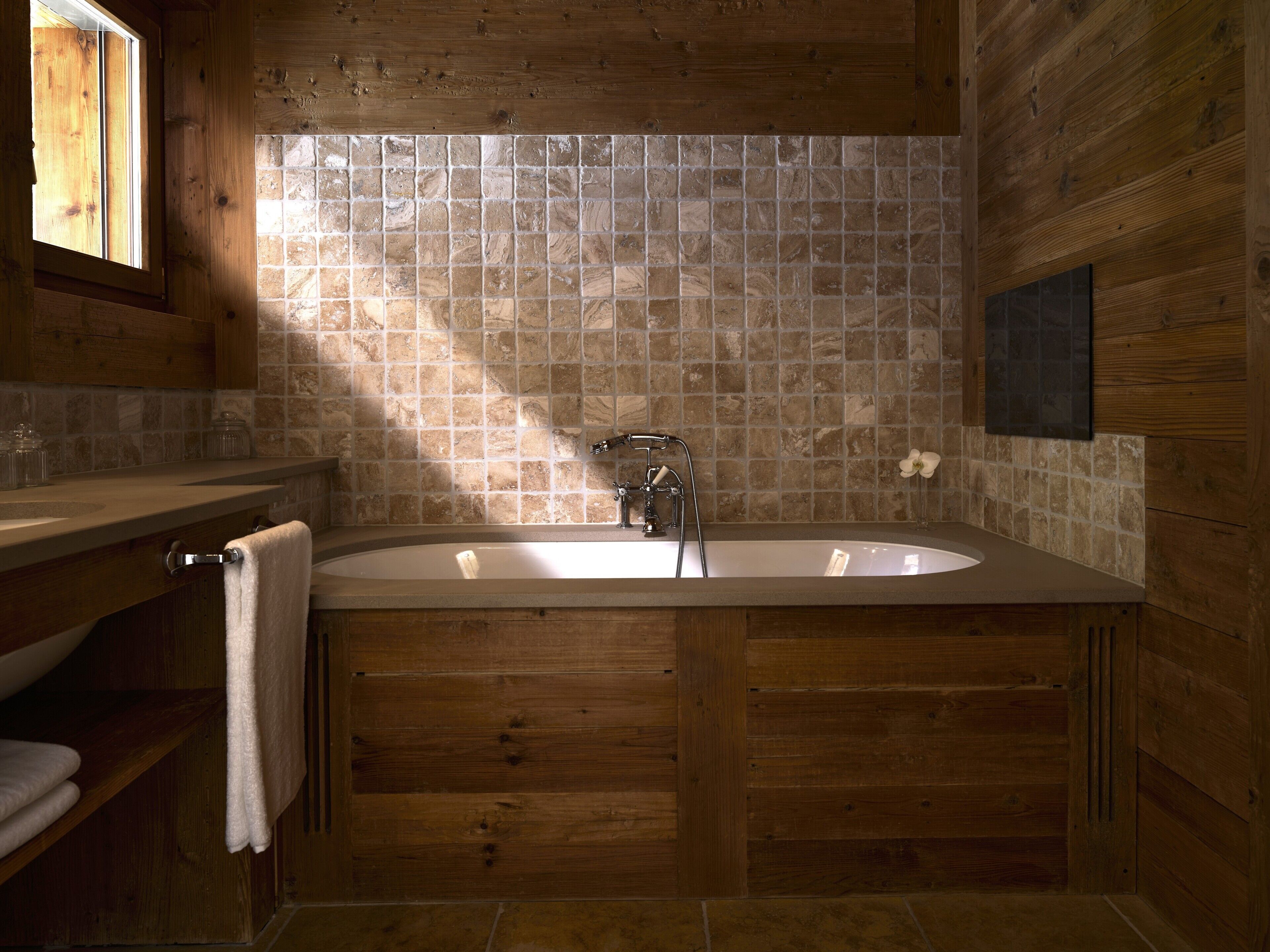 A wooden bathroom with a freestanding bathtub, a window, and a tiled wall.