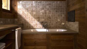 A wooden bathroom with a freestanding bathtub, a window, and a tiled wall.