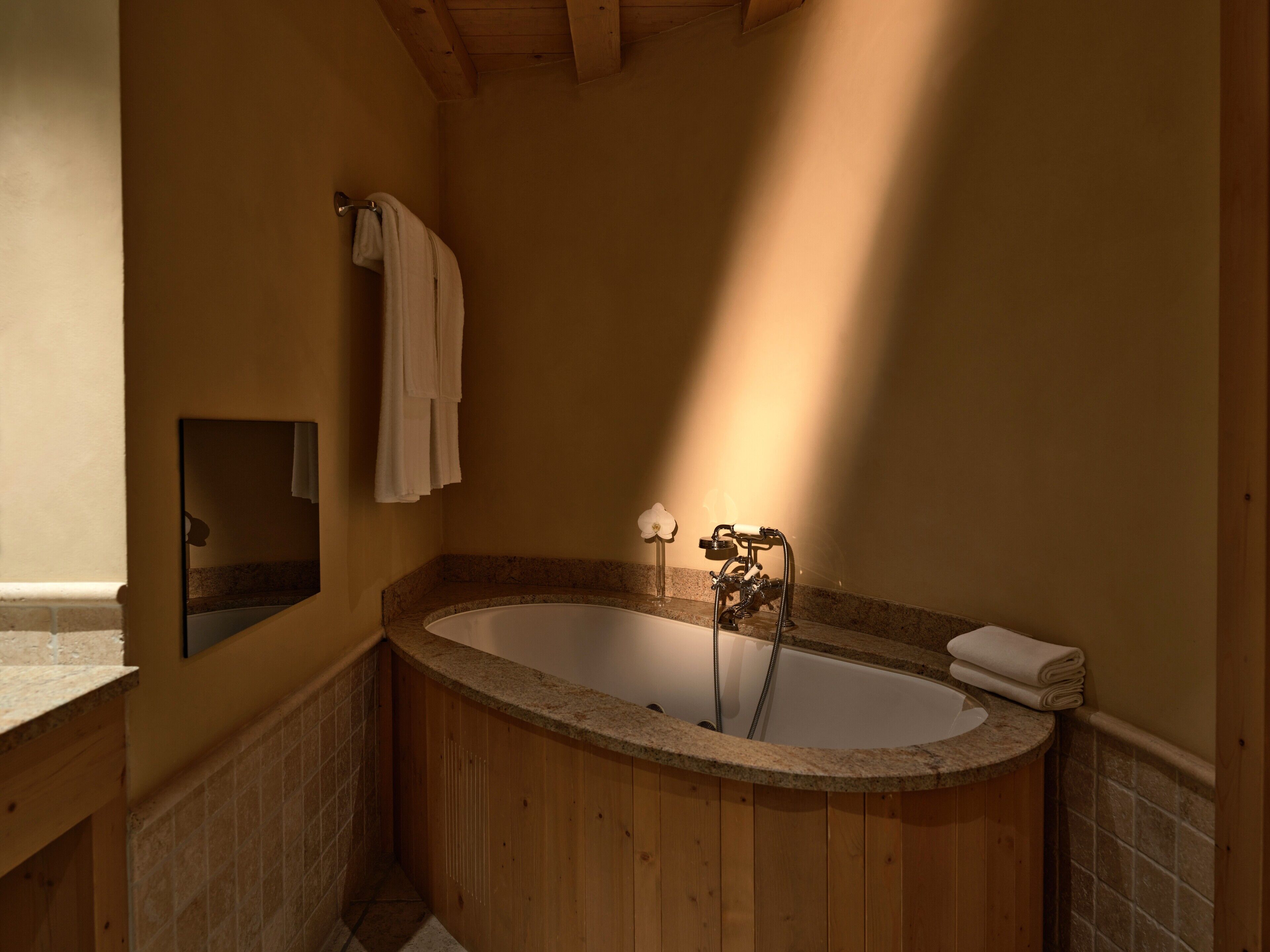 A wooden bathtub with a marble surround, a towel rack, and a small mirror on the wall.