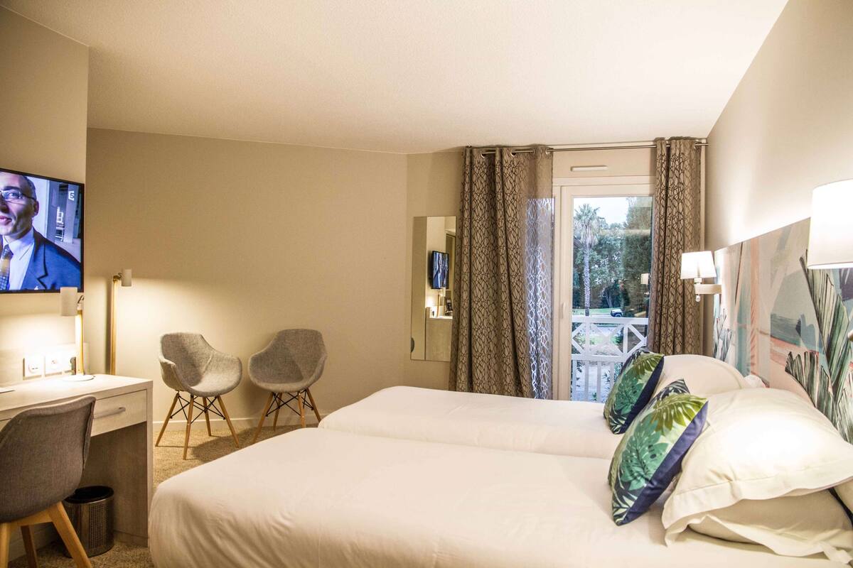 A hotel room with a bed, a desk, two chairs, a TV, and a view of the outdoors.