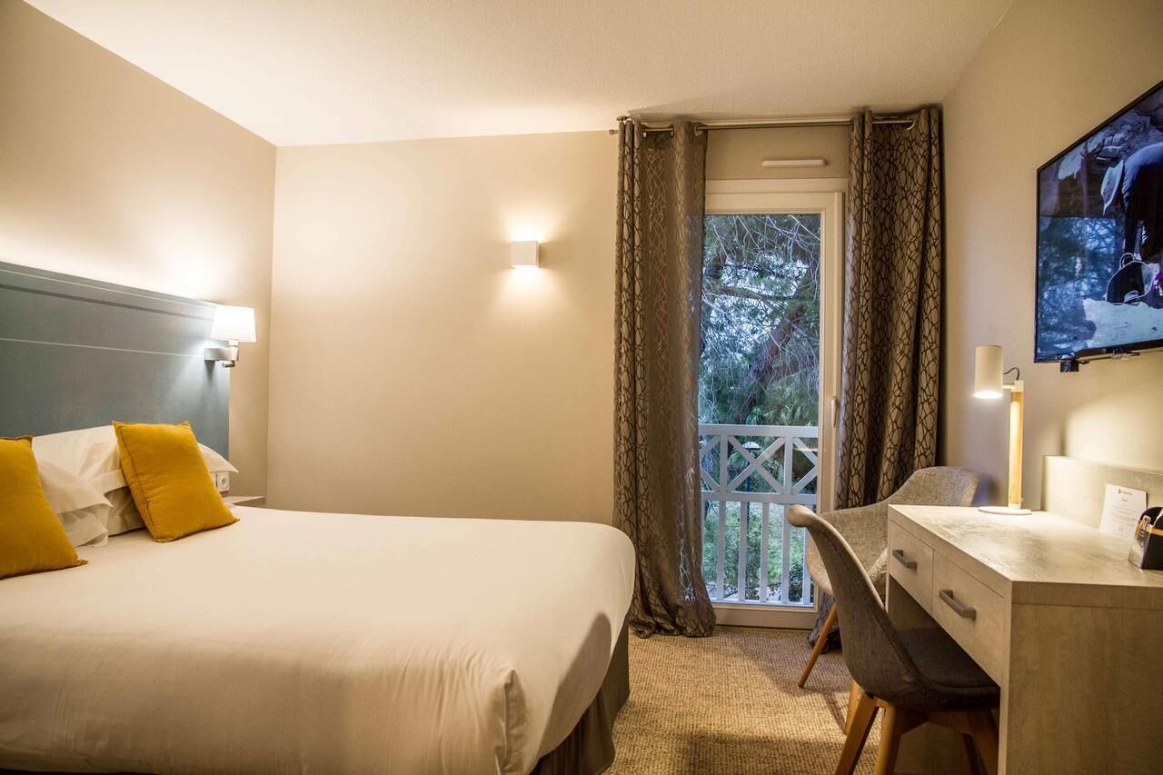 Une chambre d’hôtel avec un lit, un bureau, une chaise, une télévision et un balcon avec des rideaux.