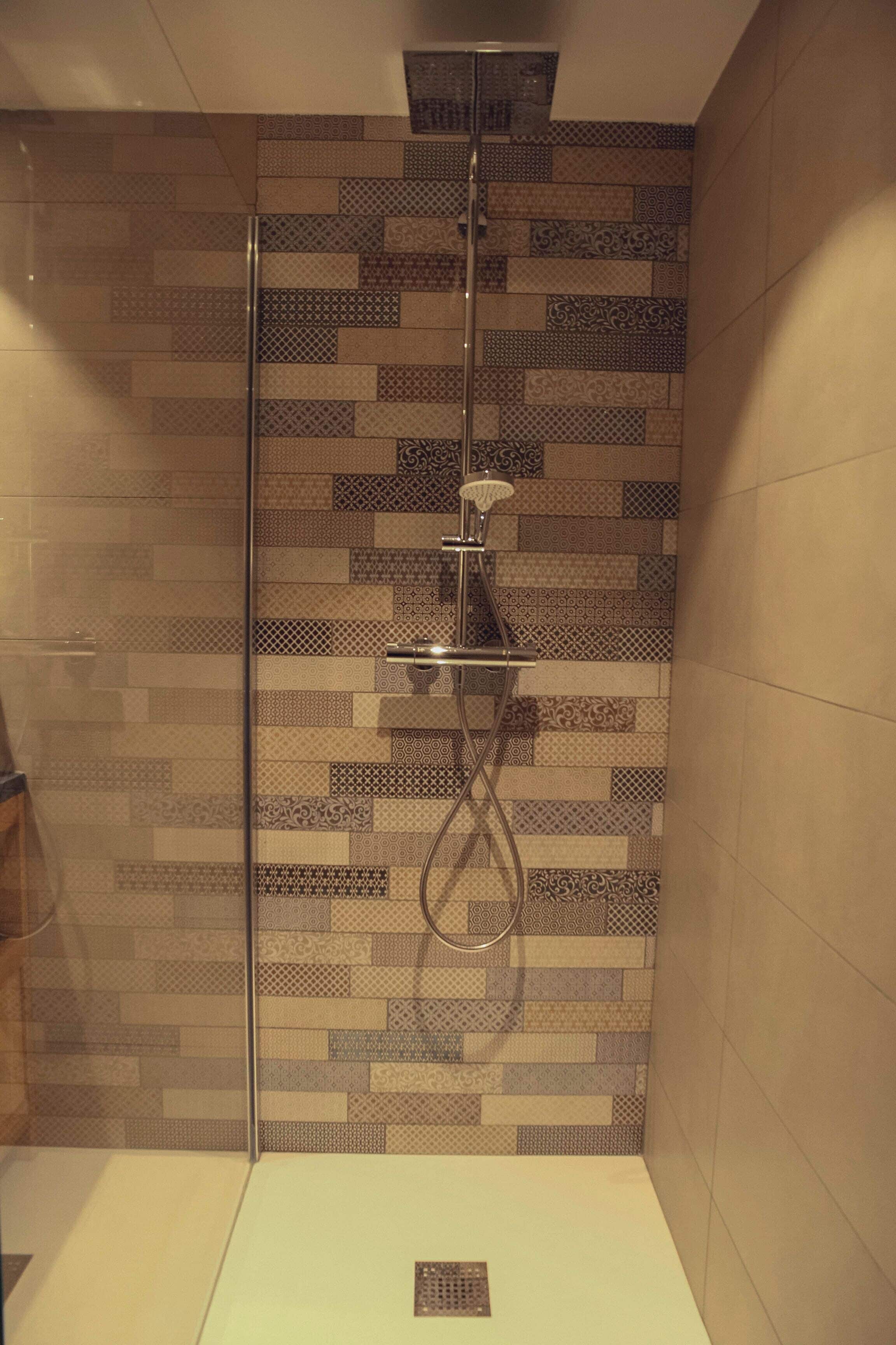 A shower with a glass door and a tiled wall with various patterns.