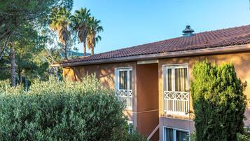 A two-story building with a tiled roof, a balcony with a railing, and a window with a lattice design.