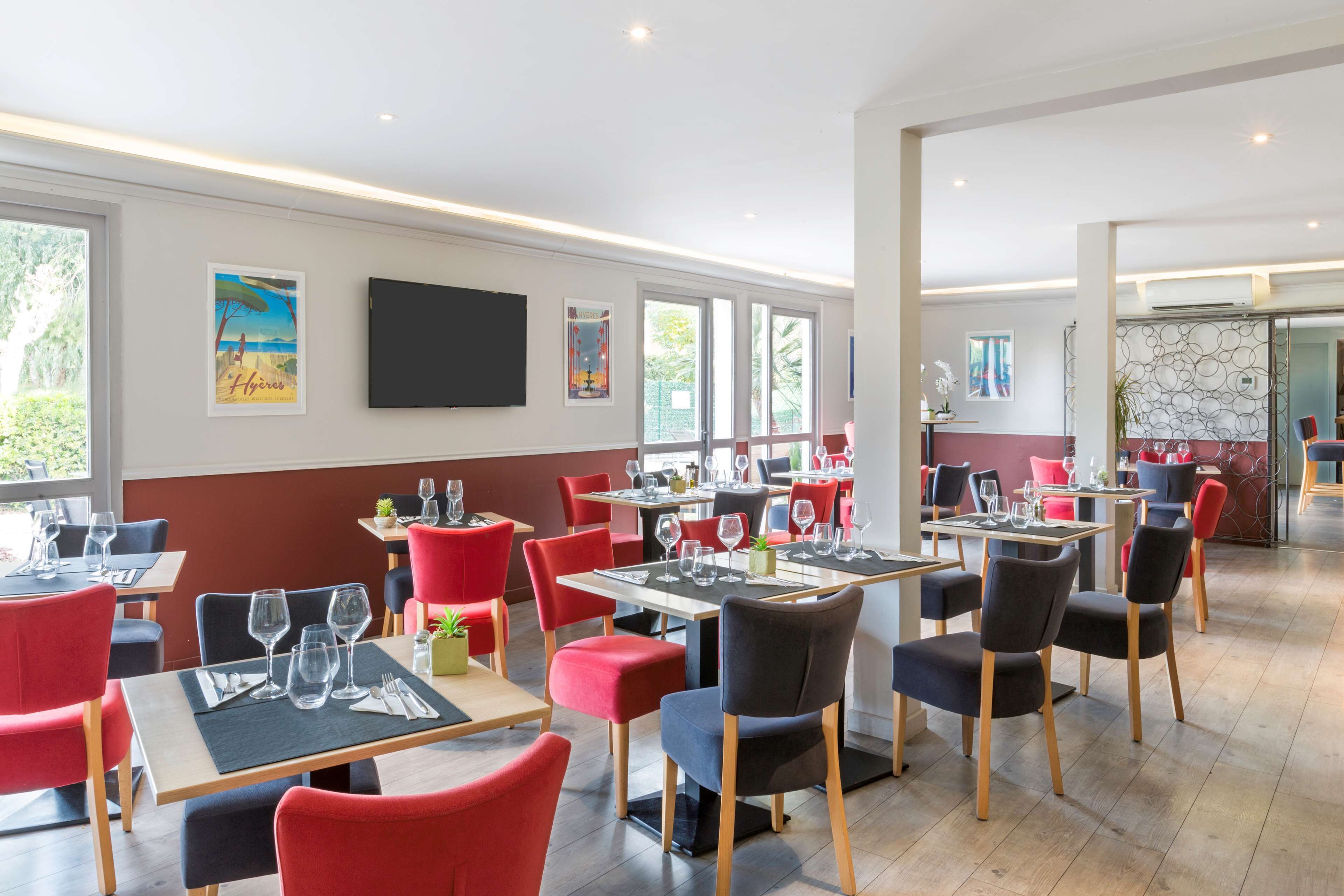 A restaurant with tables and chairs, a TV mounted on the wall, and artwork on the walls.
