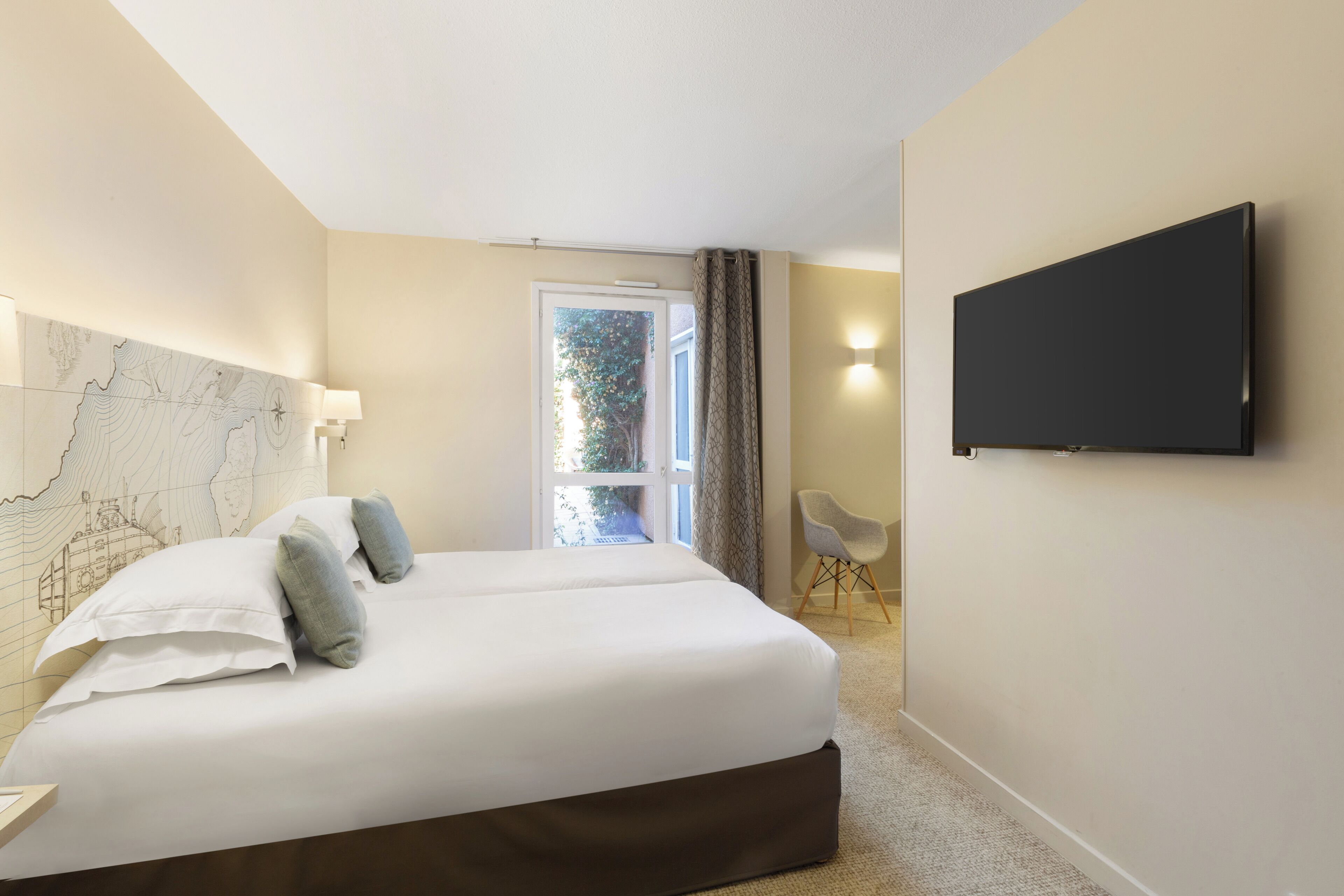 A hotel room with a large bed, a flat-screen TV mounted on the wall, and a window with curtains.