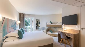 Habitación de hotel con una cama grande, un escritorio con silla, televisión y balcón con vista a zonas verdes.
