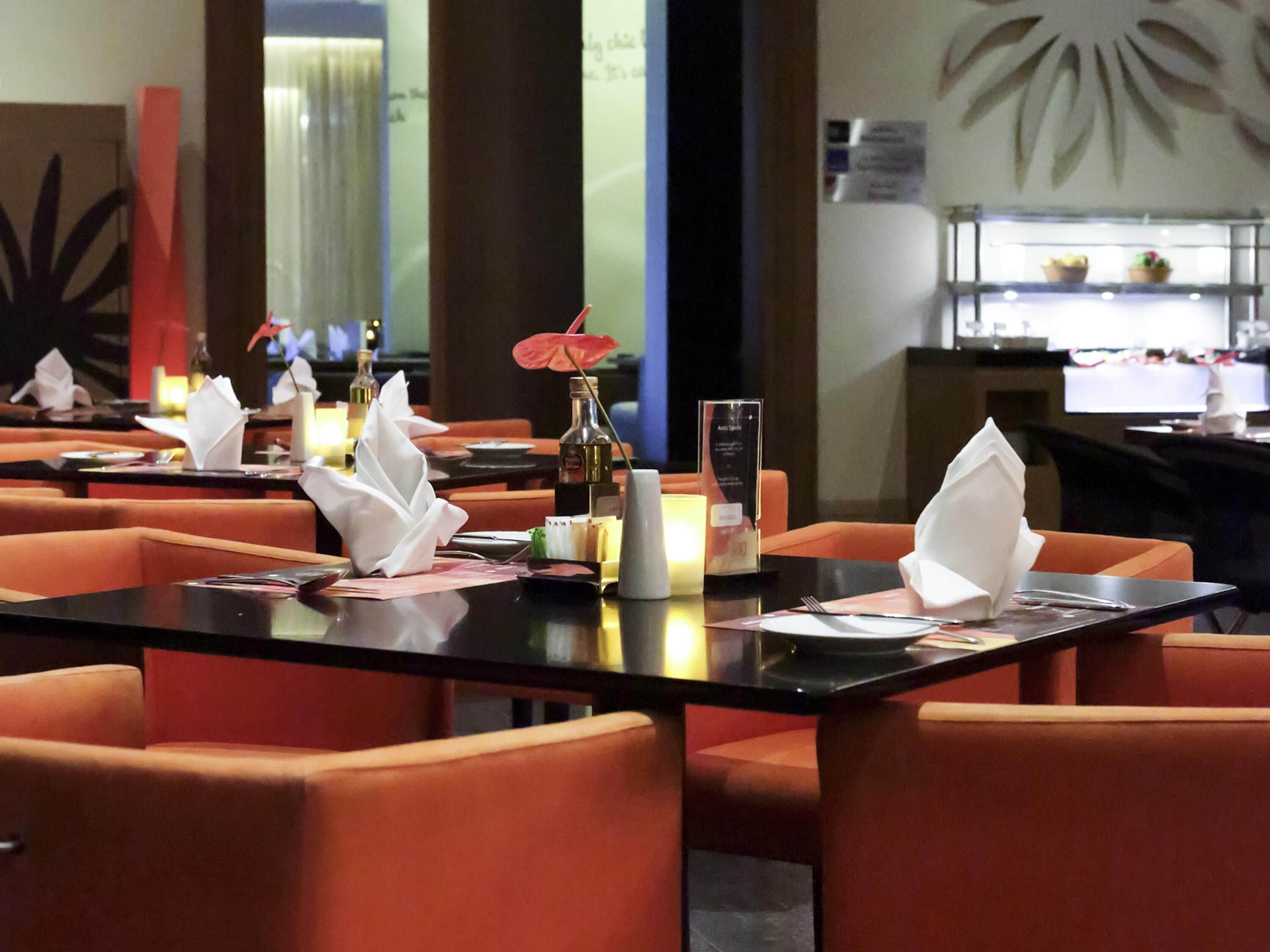 A restaurant with orange chairs, black tables, and white napkins.