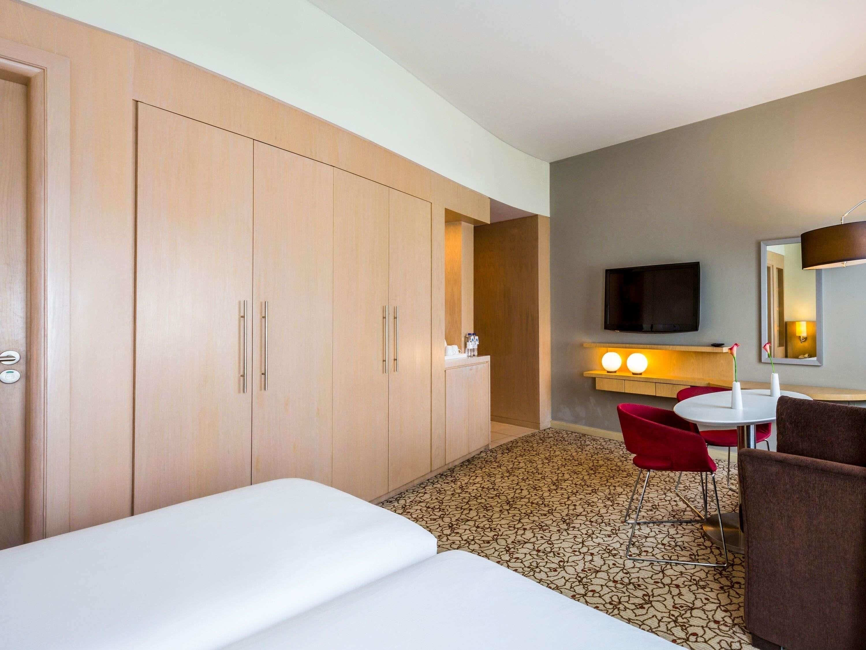Una habitación de hotel con cama, escritorio, silla, televisor y espejo.