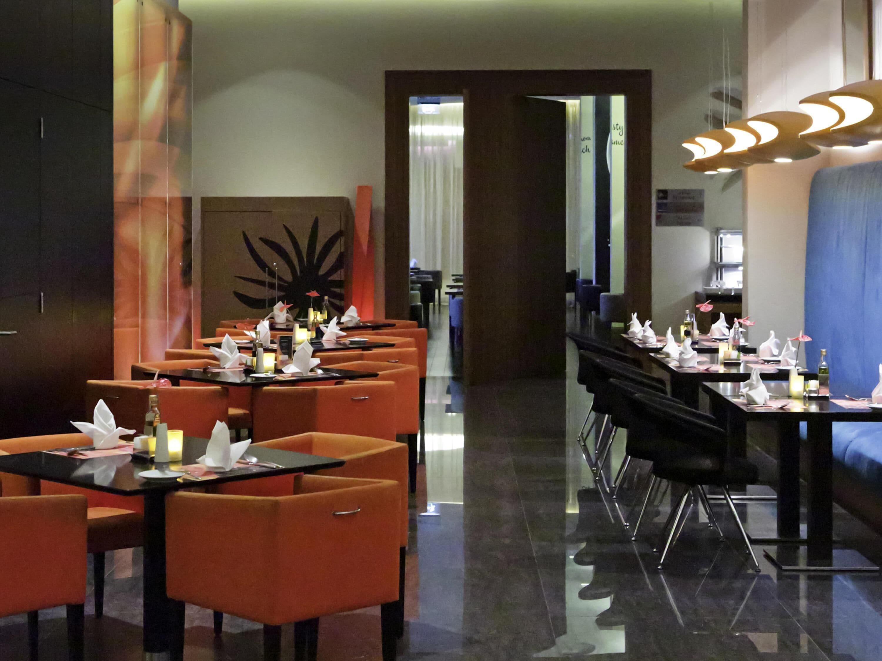 Un restaurant moderne avec des chaises orange et des tables noires, doté d’un long comptoir et d’un mur décoratif.