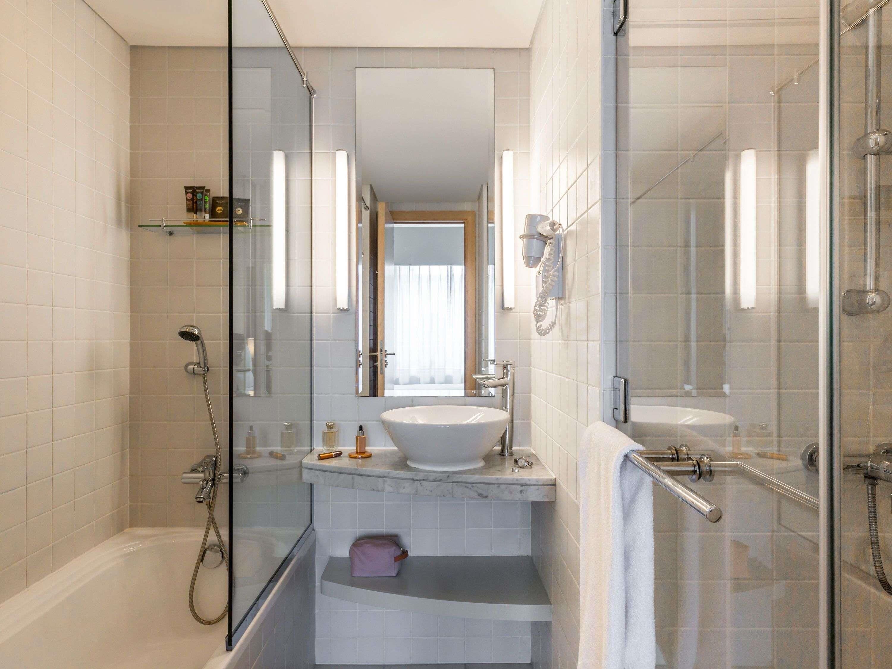Une salle de bain moderne avec une douche à parois de verre, un grand miroir et un lavabo blanc.
