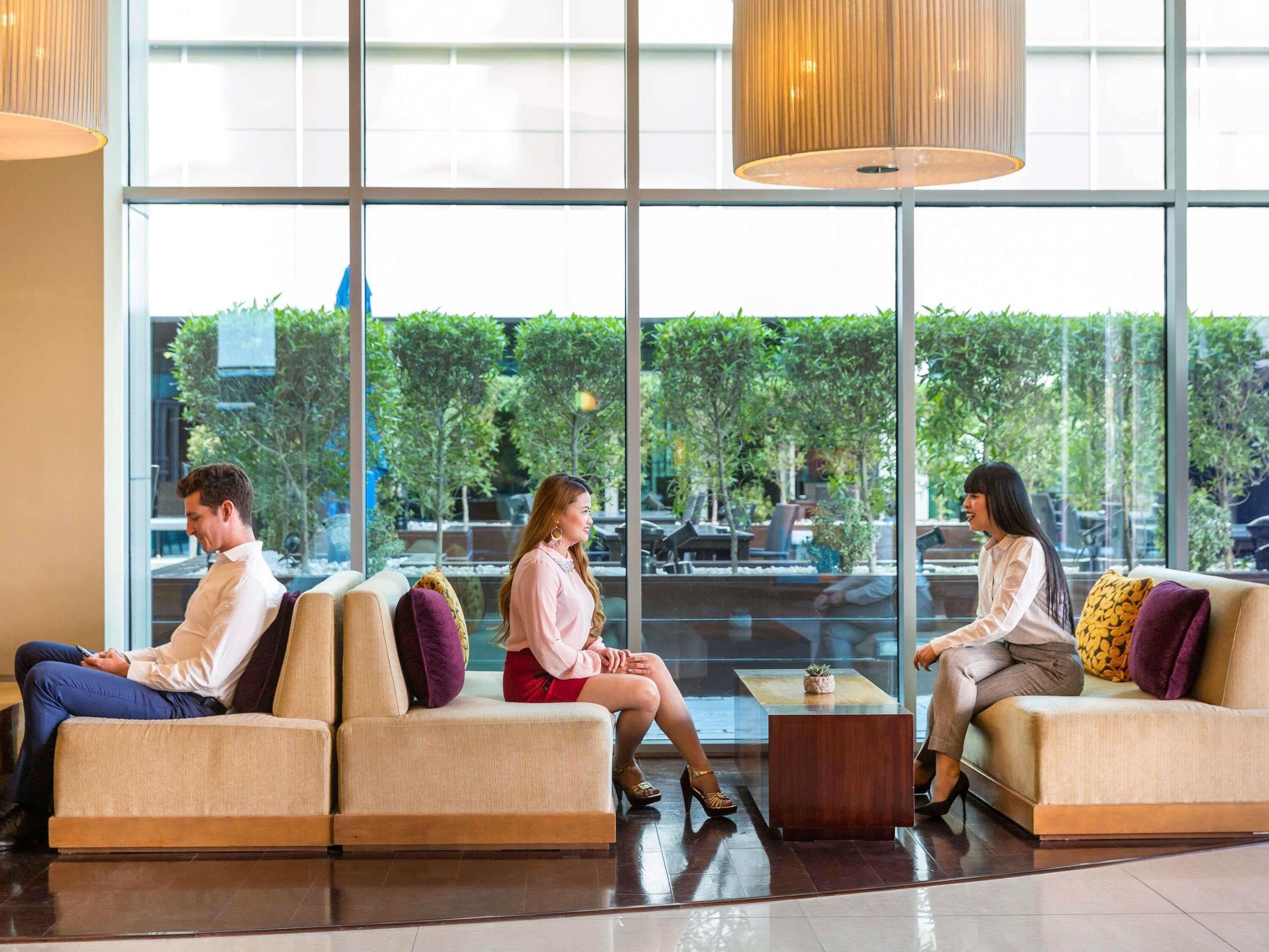 A modern lobby with three sofas, a coffee table, and large windows offering an outdoor view.