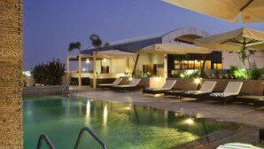 A pool area with lounge chairs and umbrellas, a clear pool, and a modern building in the background.