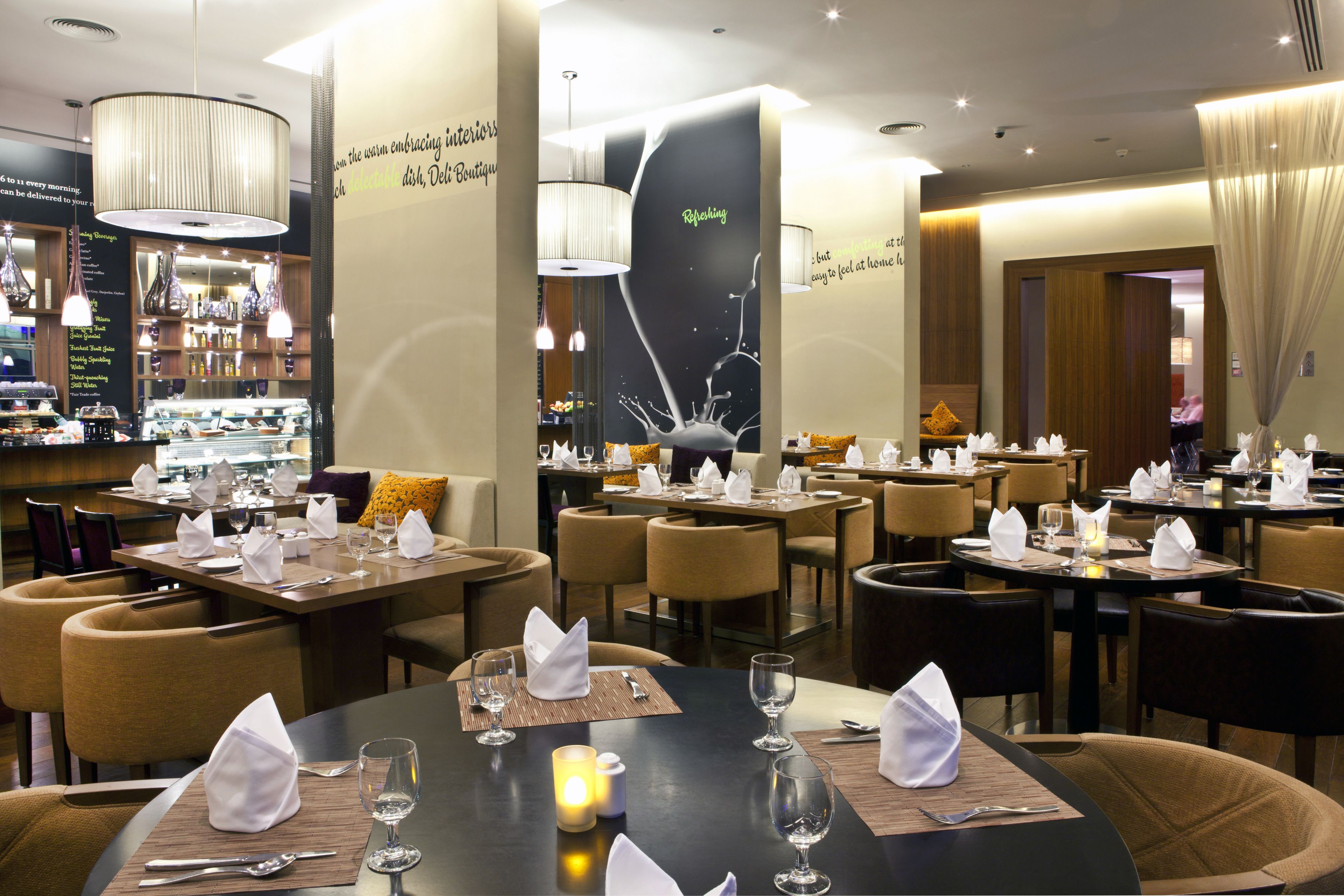 A restaurant with tables set for dining, featuring a modern interior design with pendant lighting and a wall with a reflective surface.