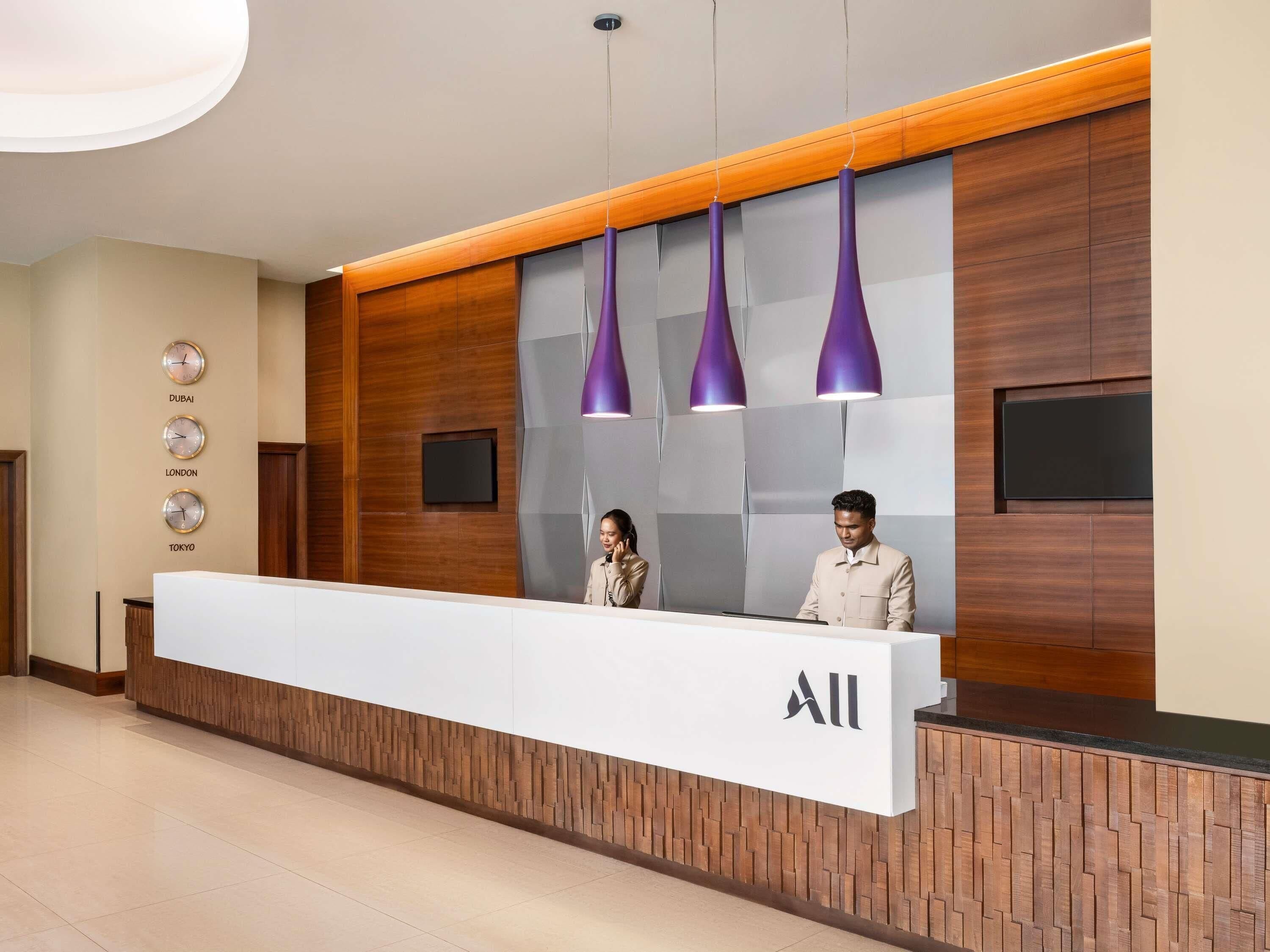 A reception desk with a modern design, featuring a wooden panel wall, a large white counter, and purple pendant lights.