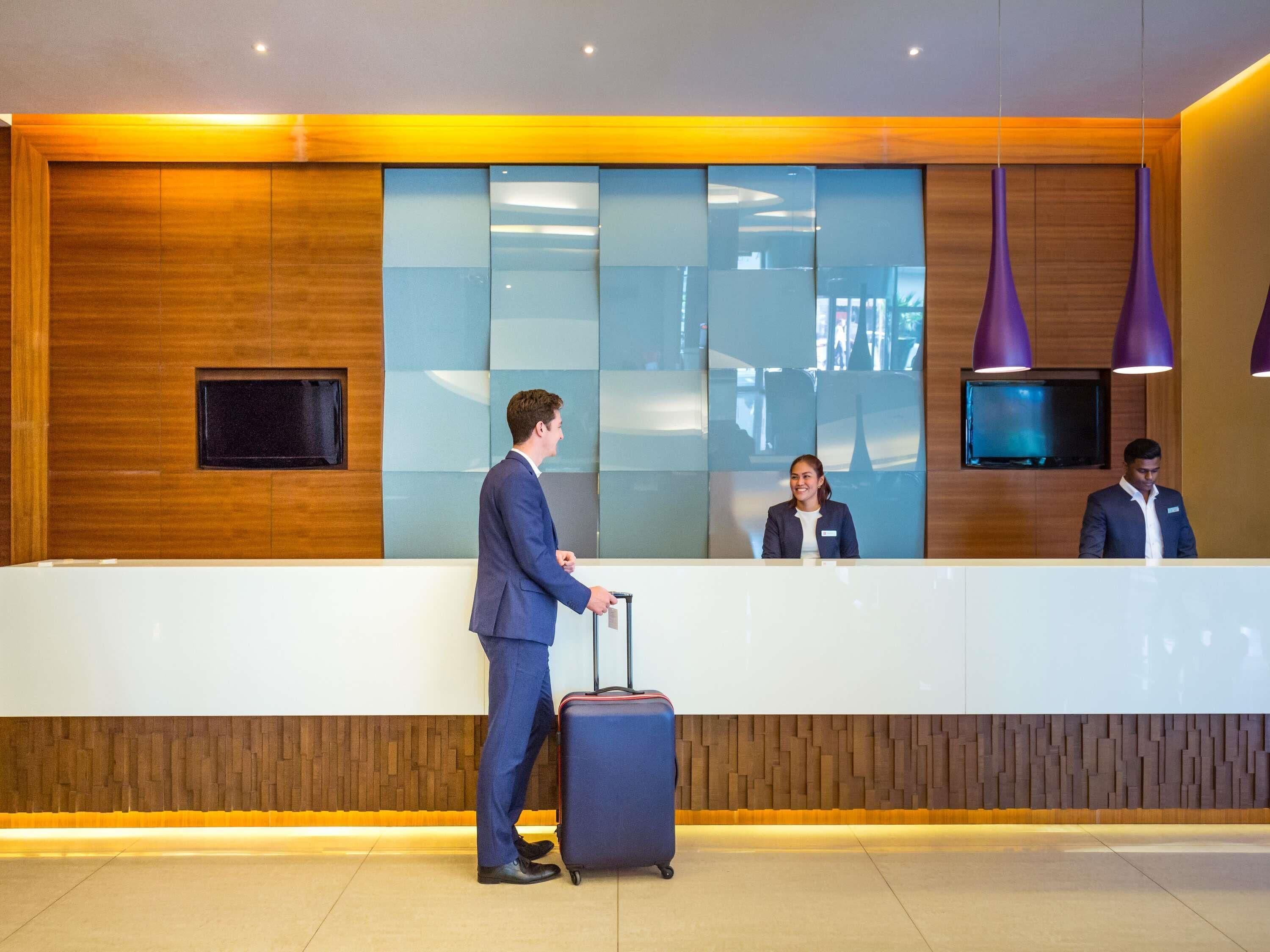 A modern hotel reception area with a wooden accent wall, a reception desk, and a television screen.