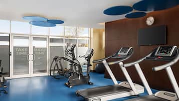 Un gimnasio con cintas de correr, elípticas y un televisor montado en la pared.