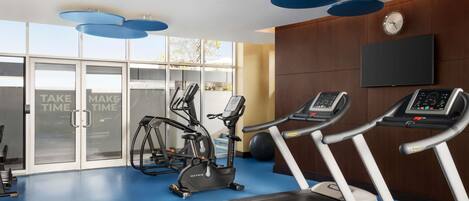Un gimnasio con cintas de correr, elípticas y un televisor montado en la pared.