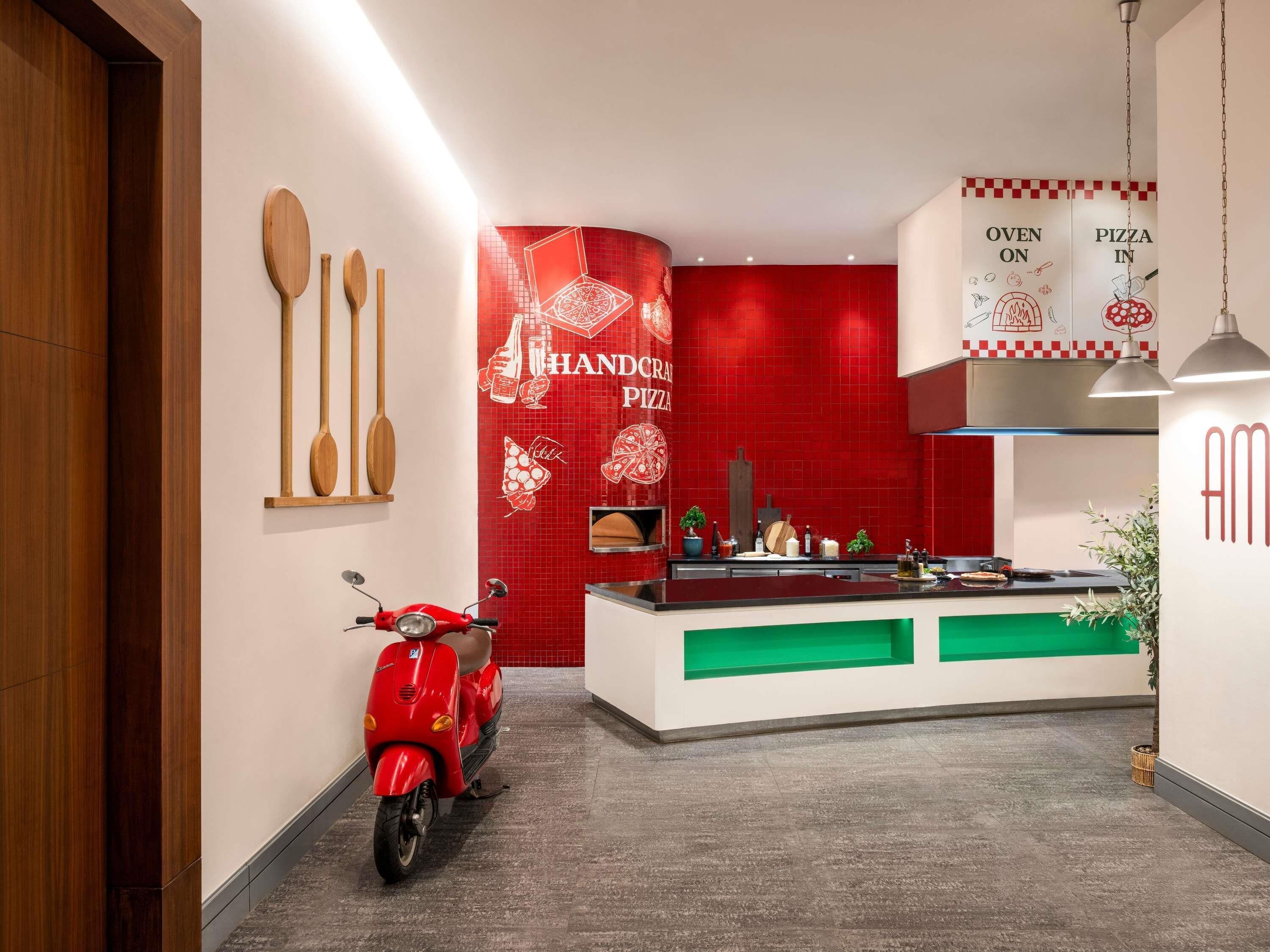 Une cuisine moderne avec un mur de crédence rouge, un scooter rouge et une enseigne indiquant « PIZZAS FAITES À LA MAIN ».