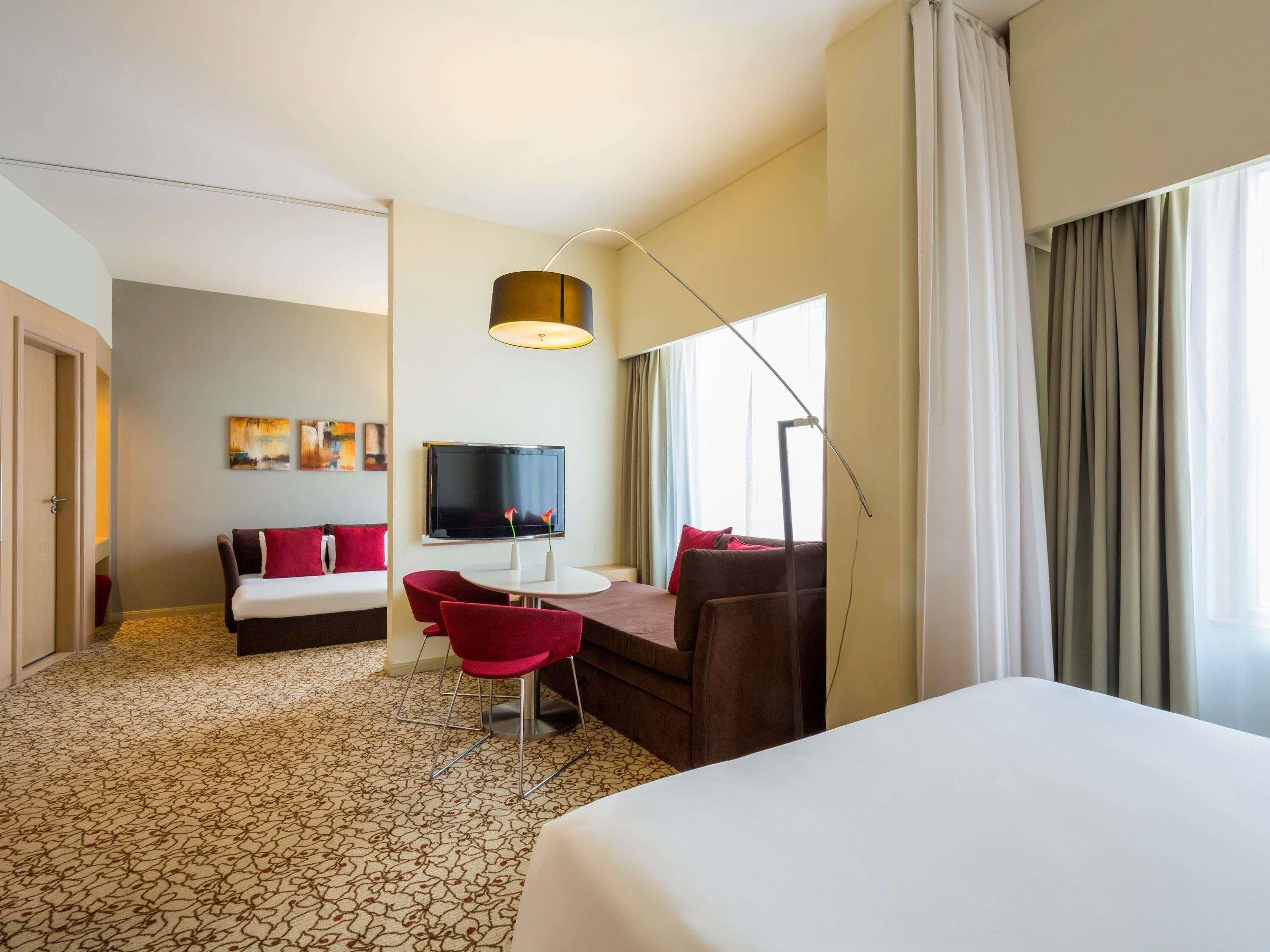 Une chambre d’hôtel comprenant un lit, un bureau avec une chaise, un canapé, une télévision et une grande fenêtre avec des rideaux.