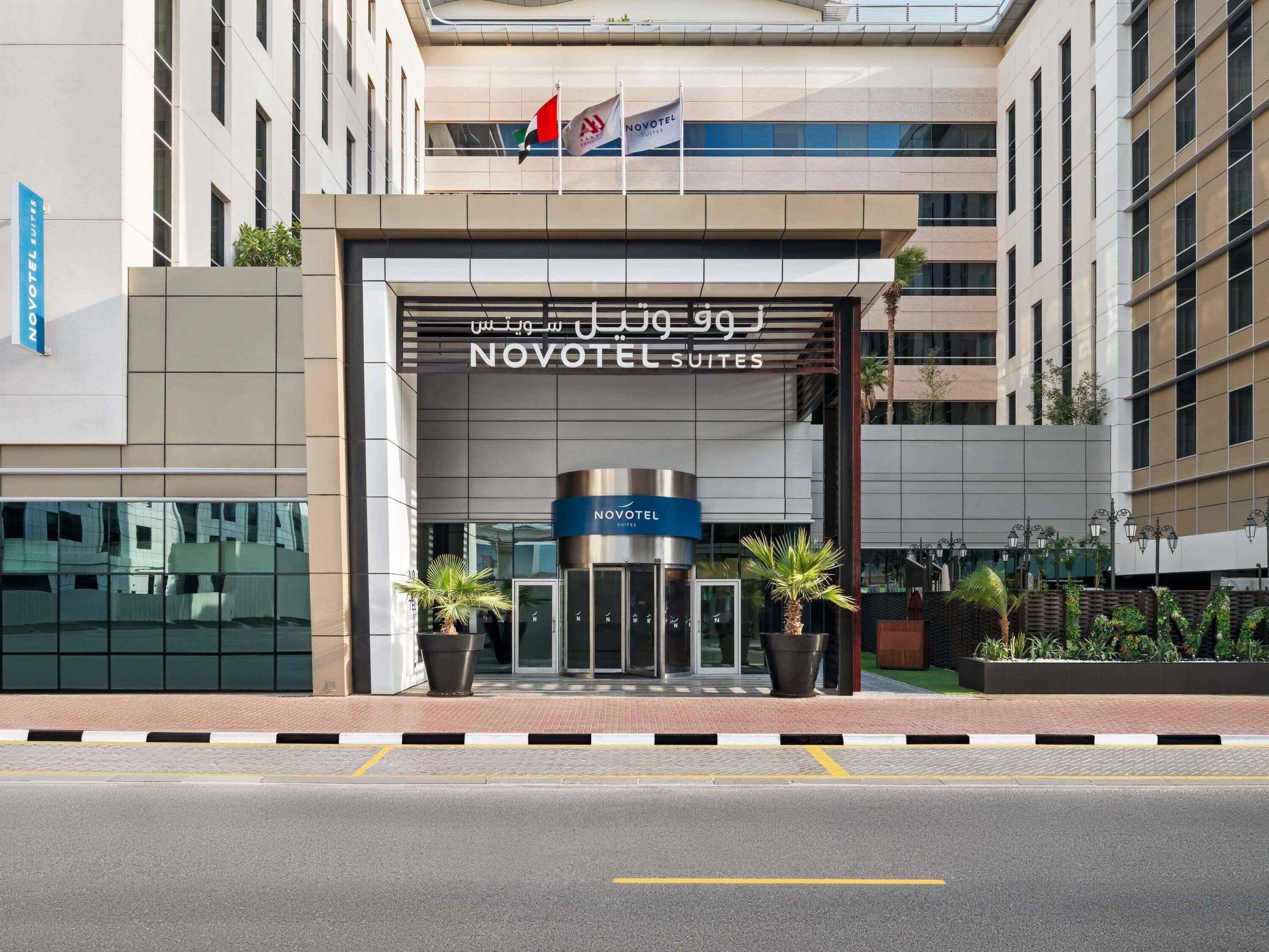 A Novotel Suites hotel entrance with a modern facade, a revolving door, and a signboard in Arabic.