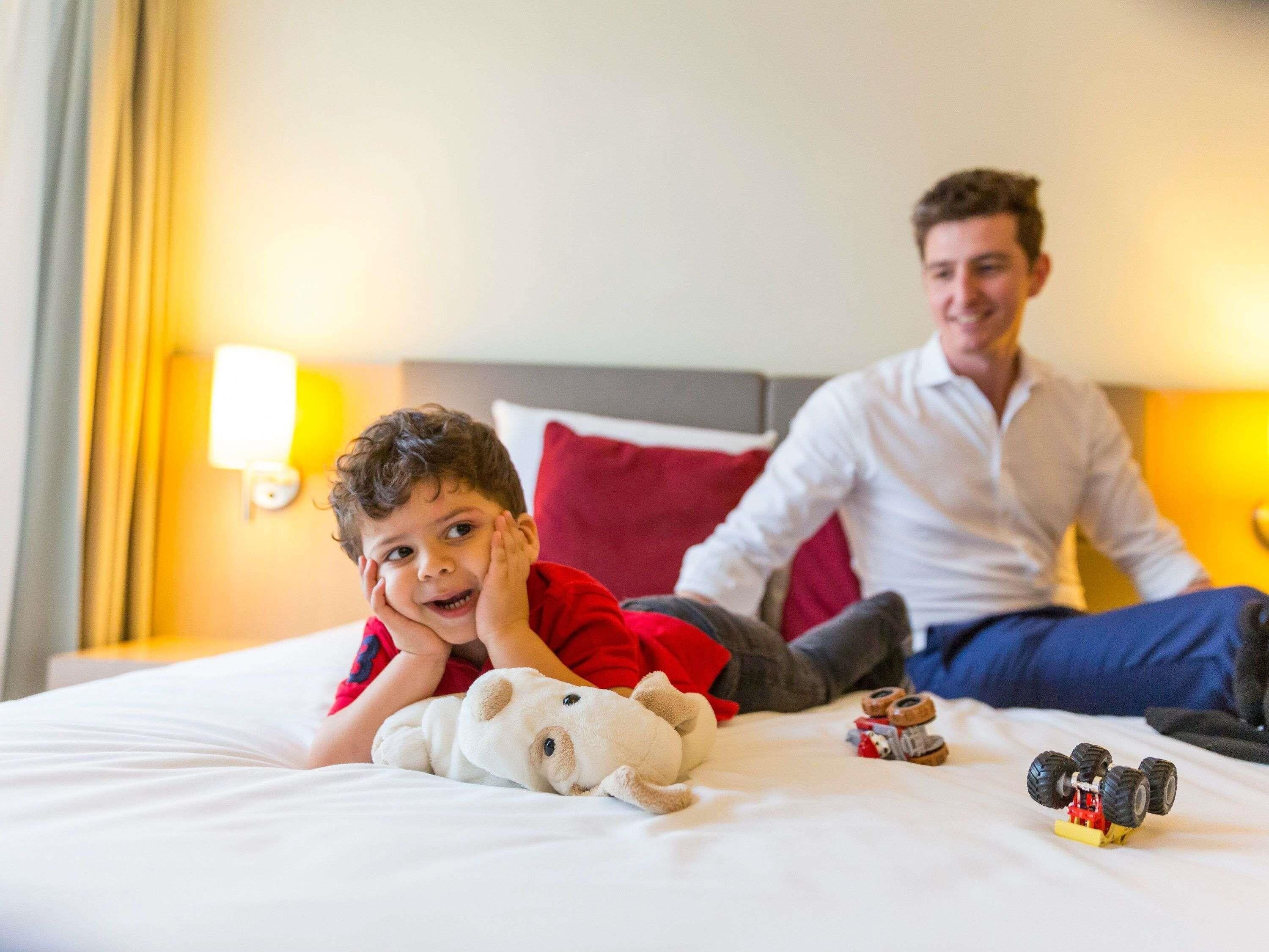 A hotel room with a bed, pillows, a lamp, and a toy car.