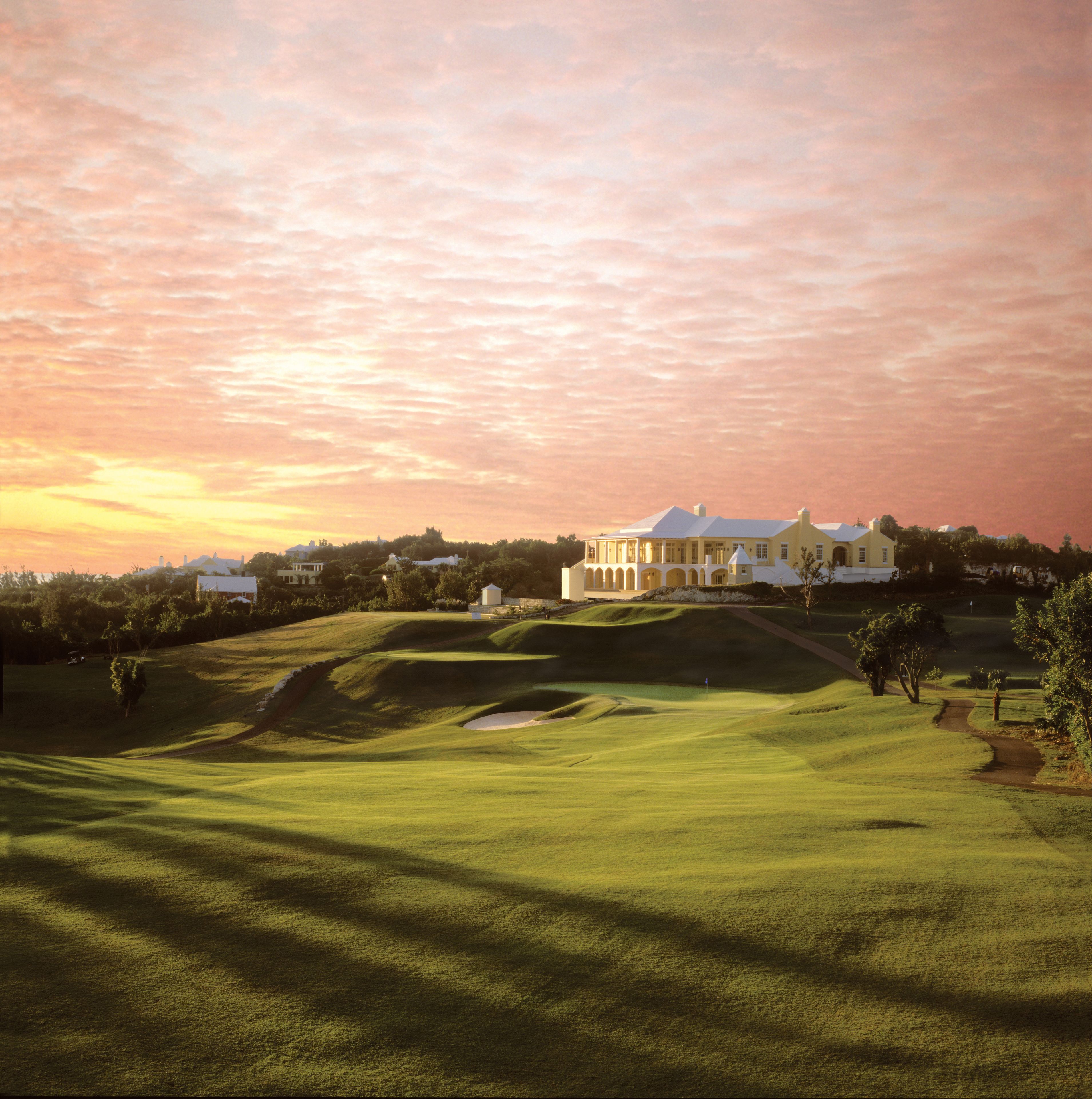 Un campo de golf con un club de campo y edificios residenciales al fondo.