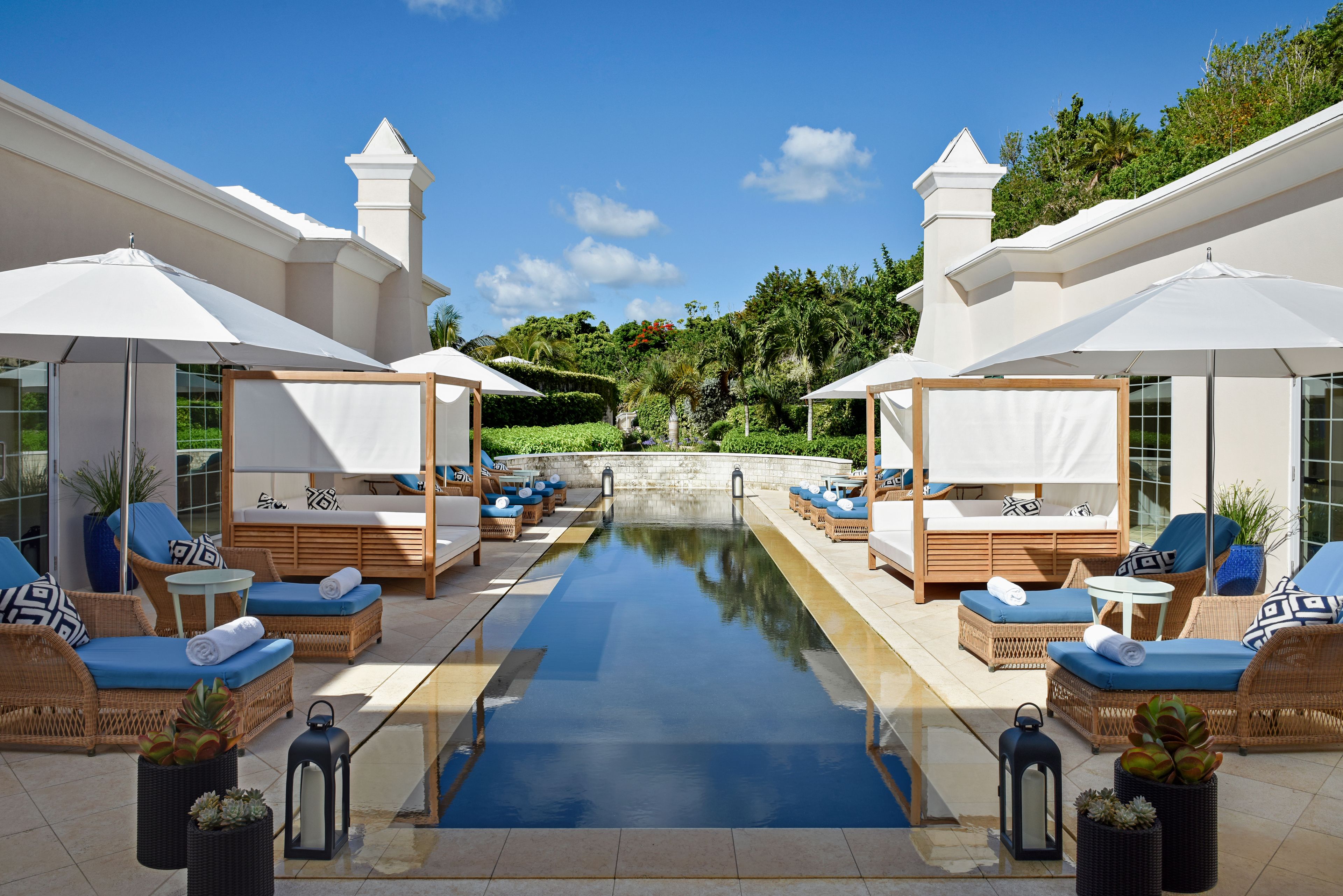 Zona de piscina con sillones de descanso y sombrillas, una piscina cristalina y vistas de la vegetación circundante.